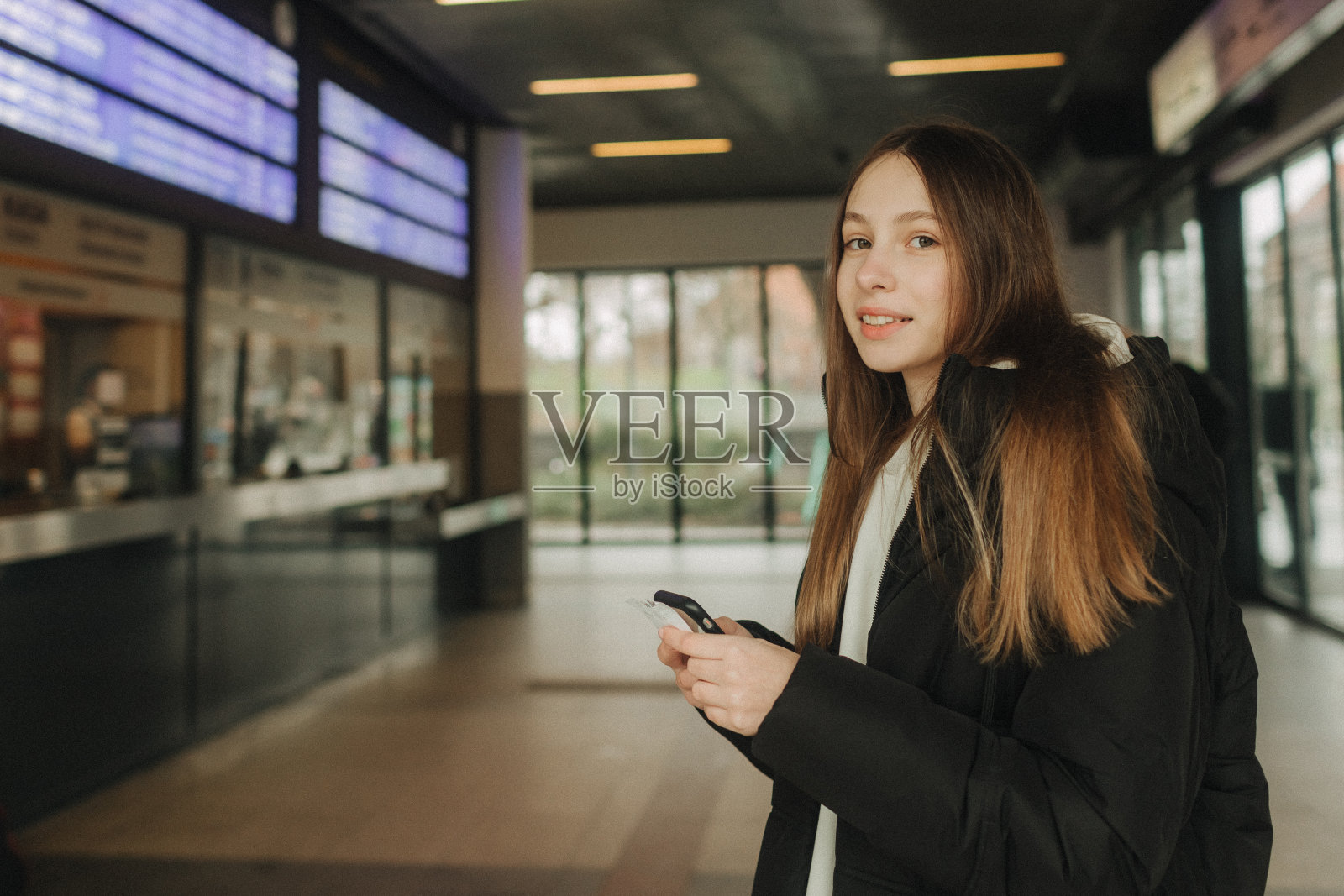 旅游少女在火车站使用智能手机地图、社交媒体签到或购票预订。现代旅游app技术，独行旅行者，寒假铁路探险概念照片摄影图片