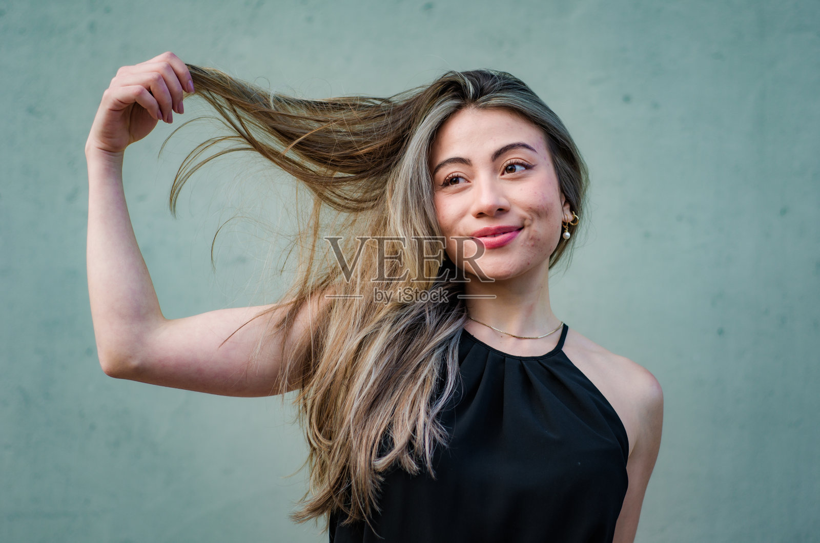 美丽的年轻女子的肖像玩她的头发在灰色背景照片摄影图片