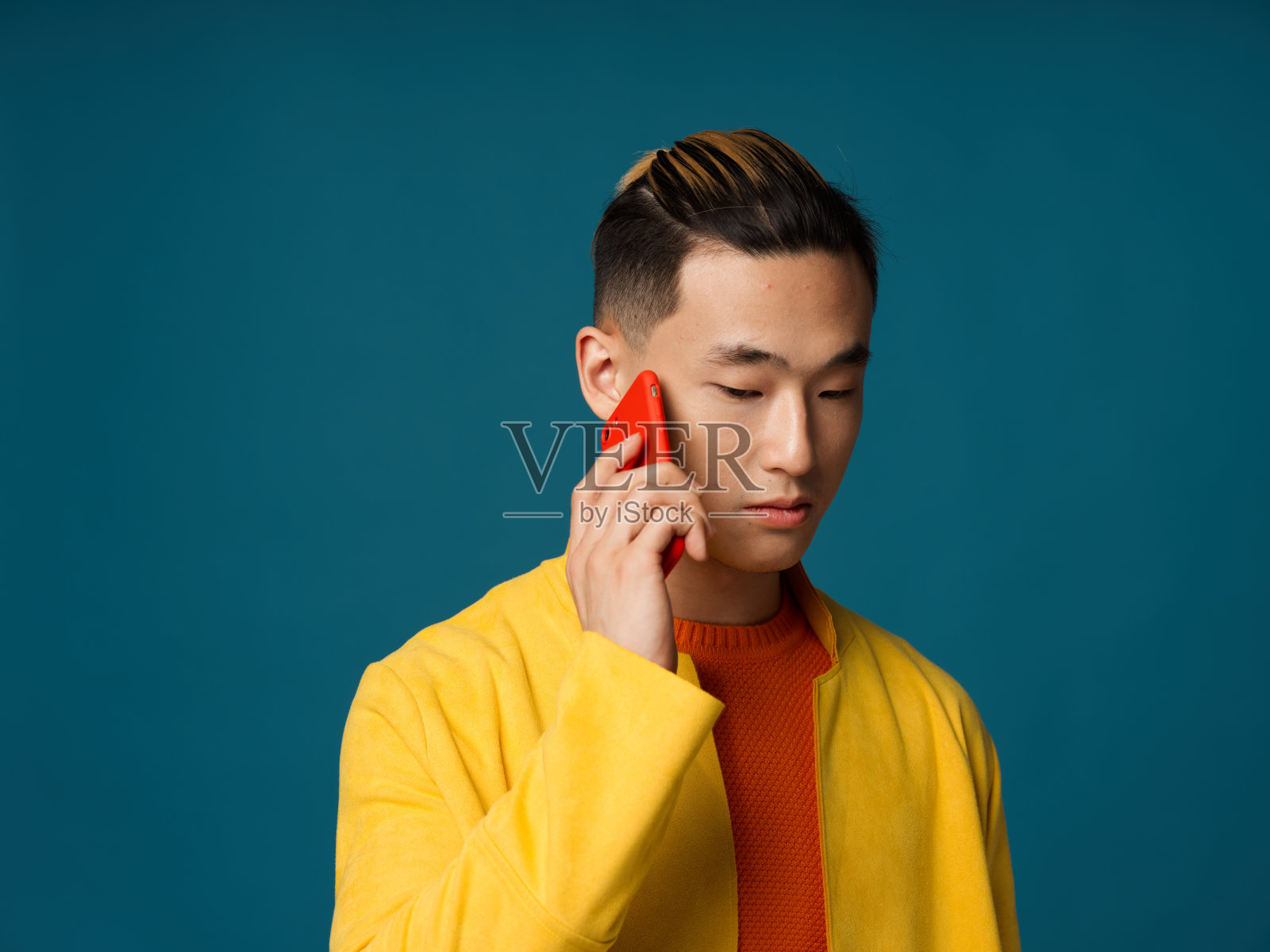 一名亚洲男子在蓝色背景下打电话，向下看裁剪过的画面照片摄影图片