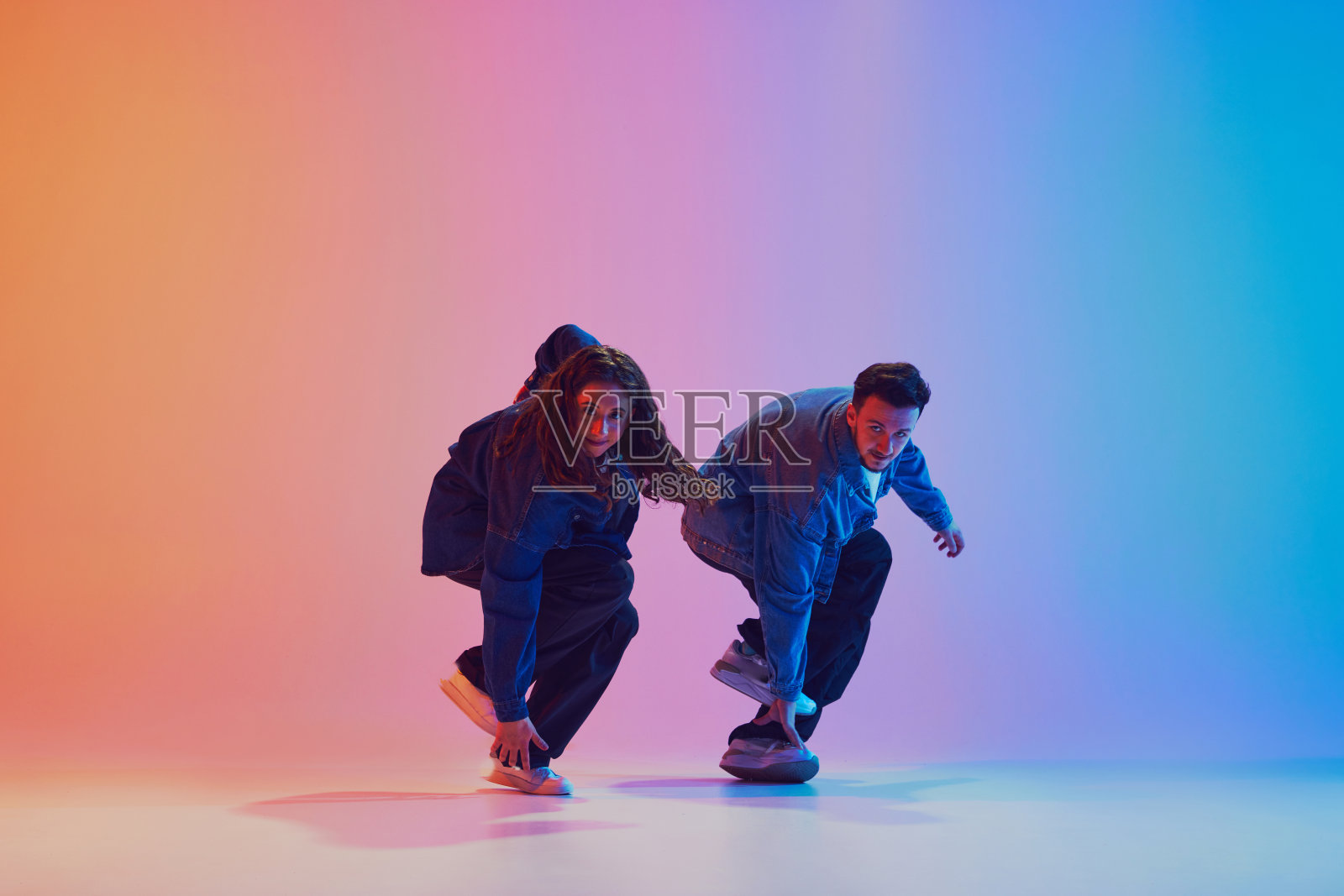 在霓虹灯的渐变背景下，两名舞者穿着牛仔服装同步表演嘻哈舞。照片摄影图片