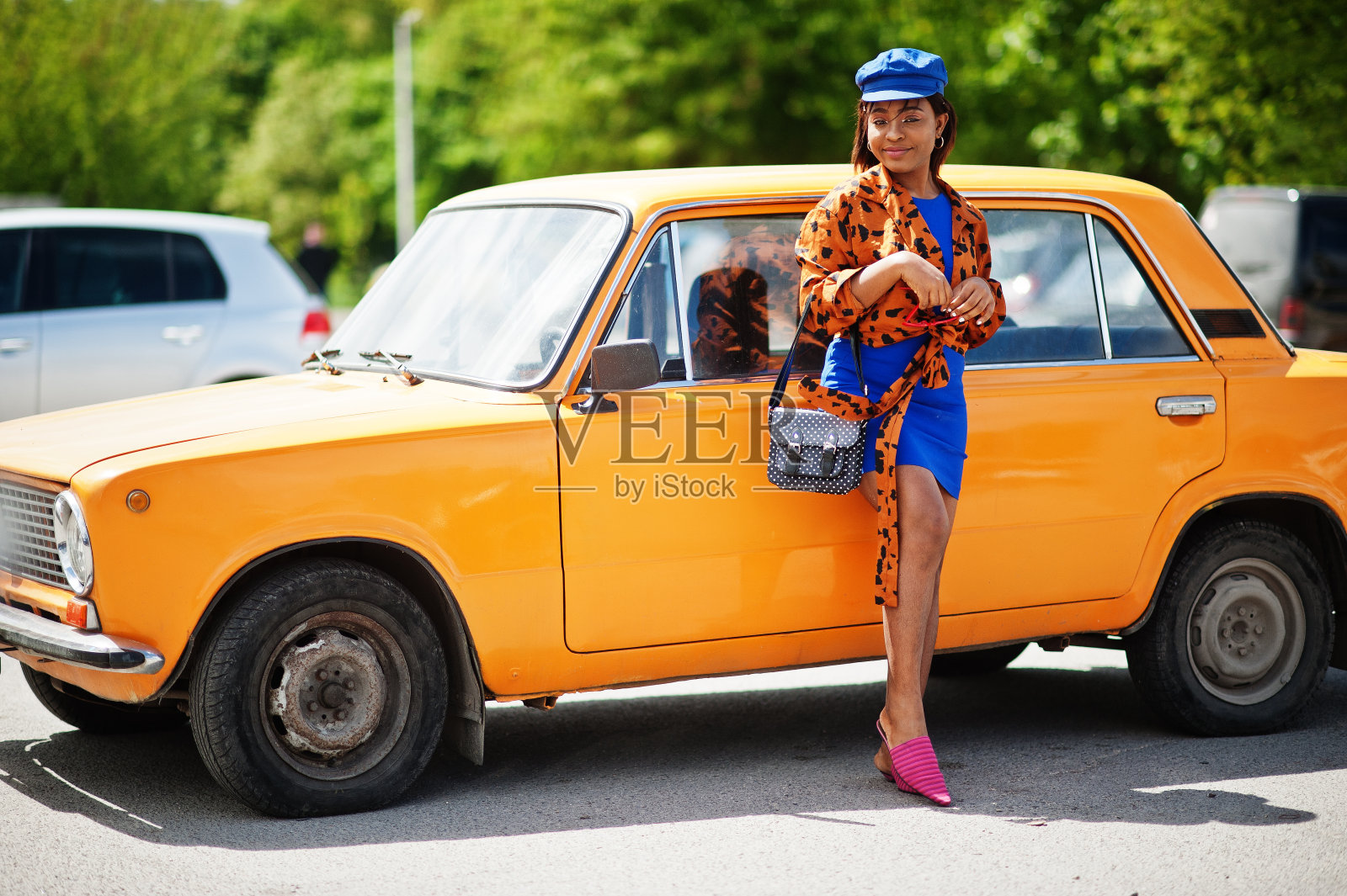 美丽的非裔美国女士站在橙色经典复古车旁。照片摄影图片
