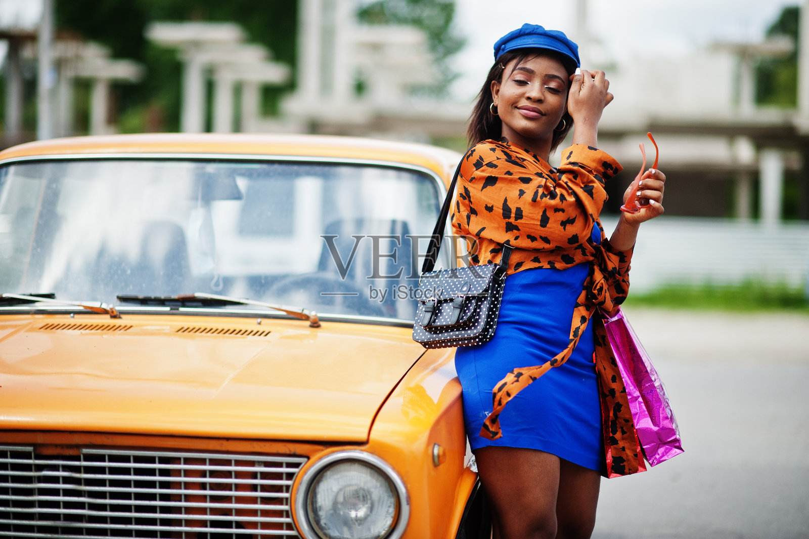 漂亮的非裔美国女士拎着购物袋站在橙色经典复古车旁。照片摄影图片