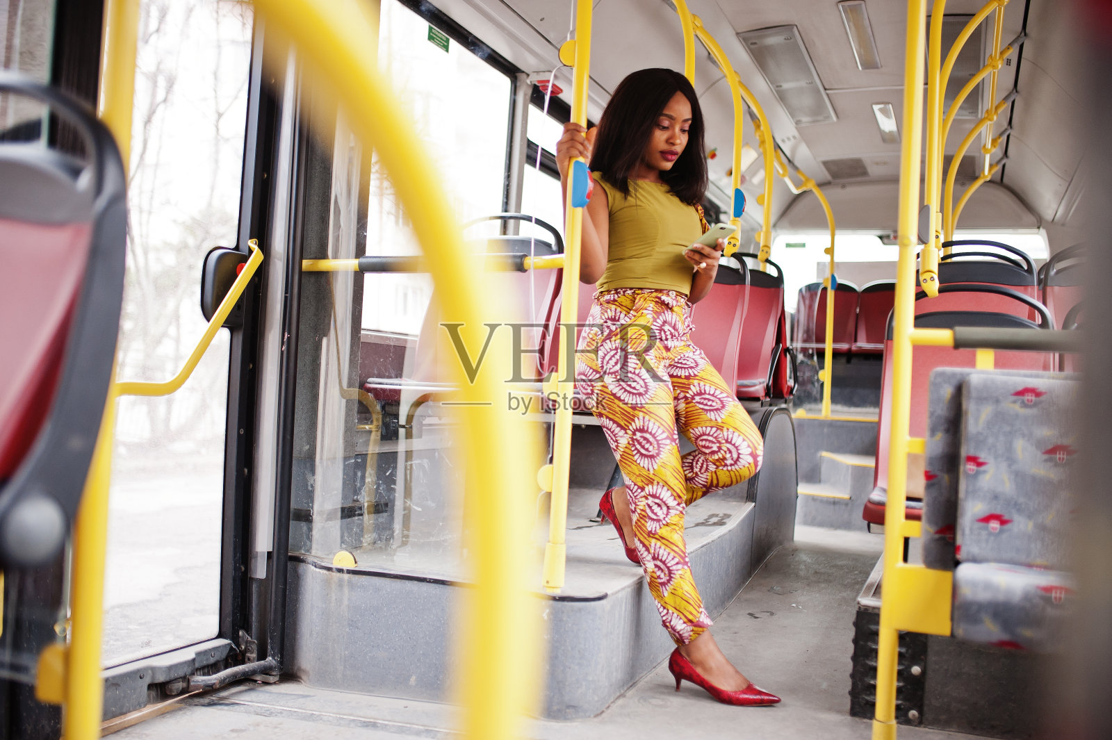 年轻时尚的非裔美国女性拿着手机坐在公共汽车上。照片摄影图片