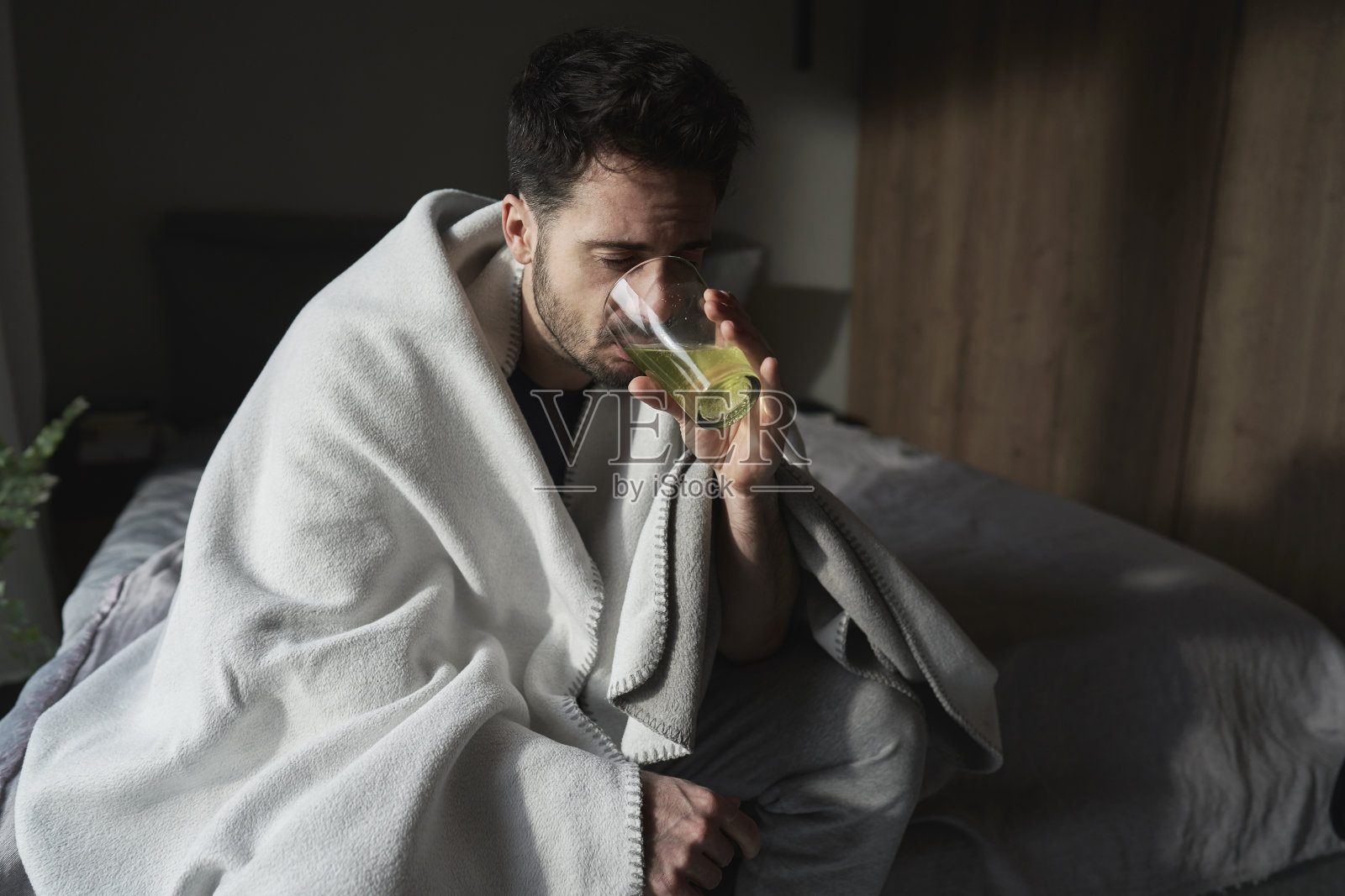 病人坐在毯子下喝着玻璃杯里的药照片摄影图片