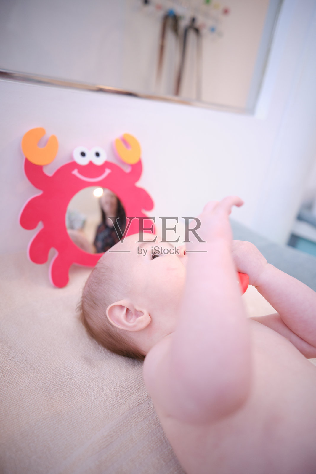 一个婴儿正在看一面镜子，镜子上有一只螃蟹。一个女人站在婴儿后面照片摄影图片