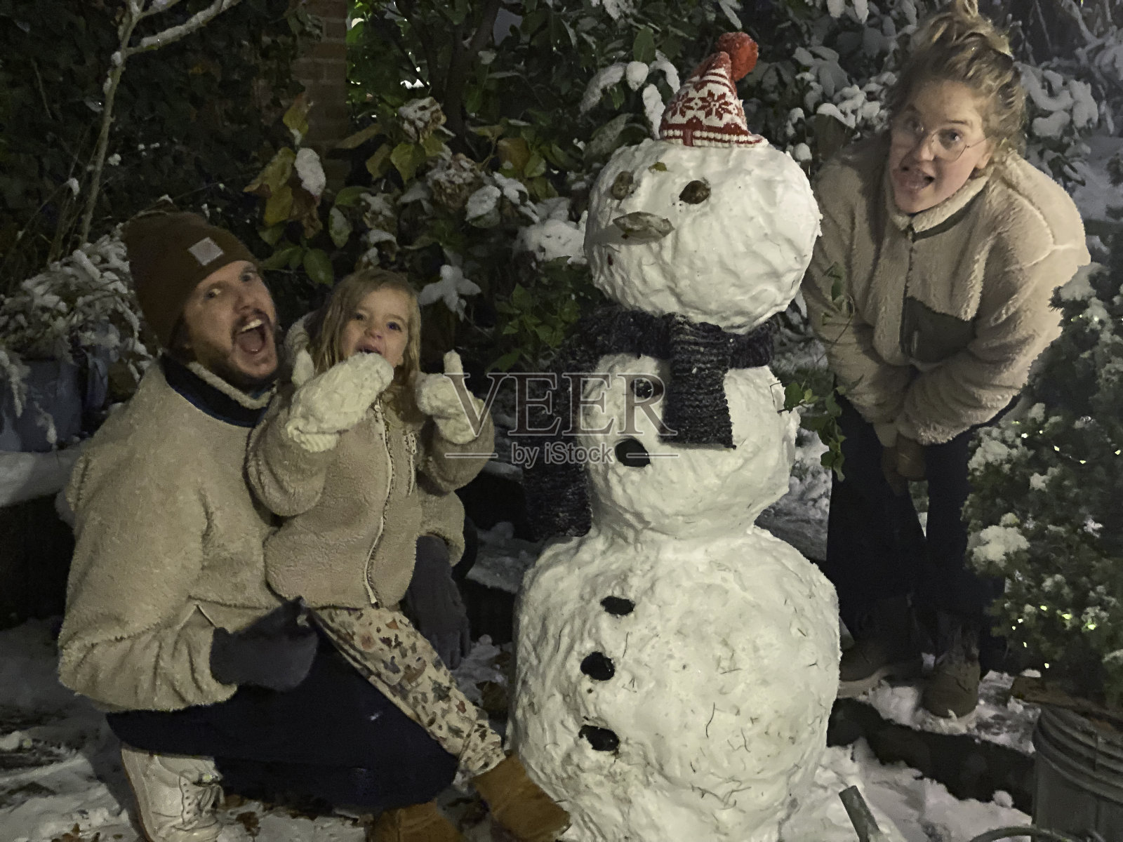 怀孕的母亲和她的家人在堆雪人。照片摄影图片