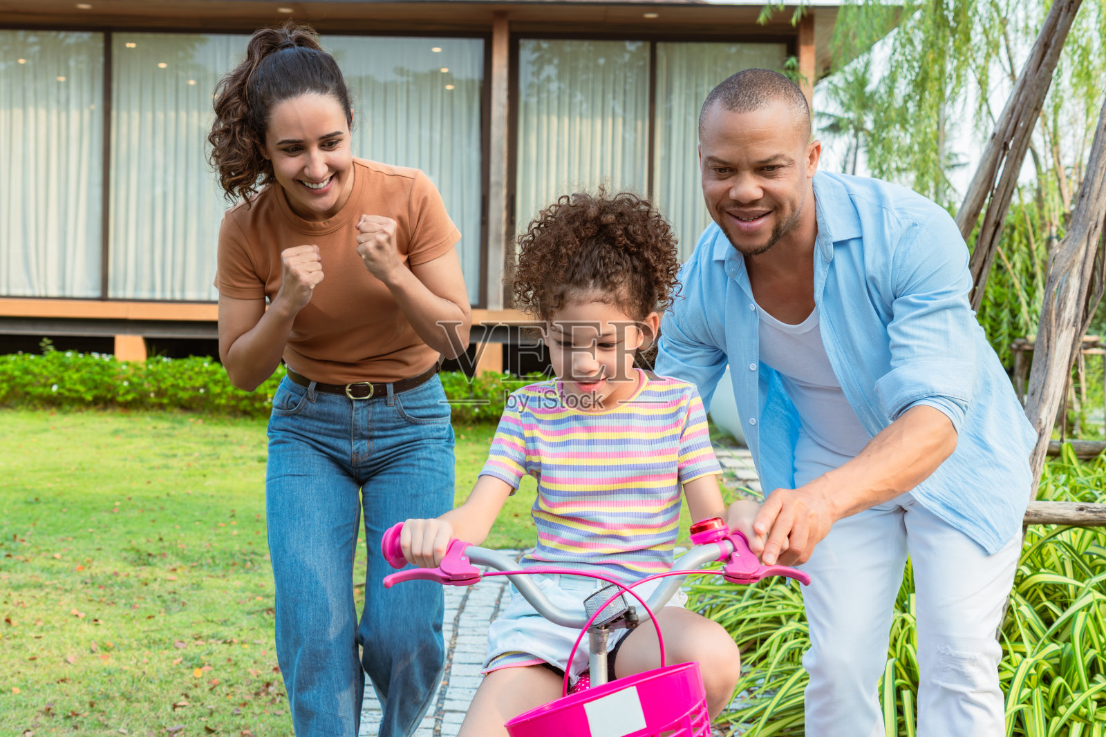 我的混血父母周末在院子里鼓励和指导我上小学的女儿进行户外自行车训练。照片摄影图片