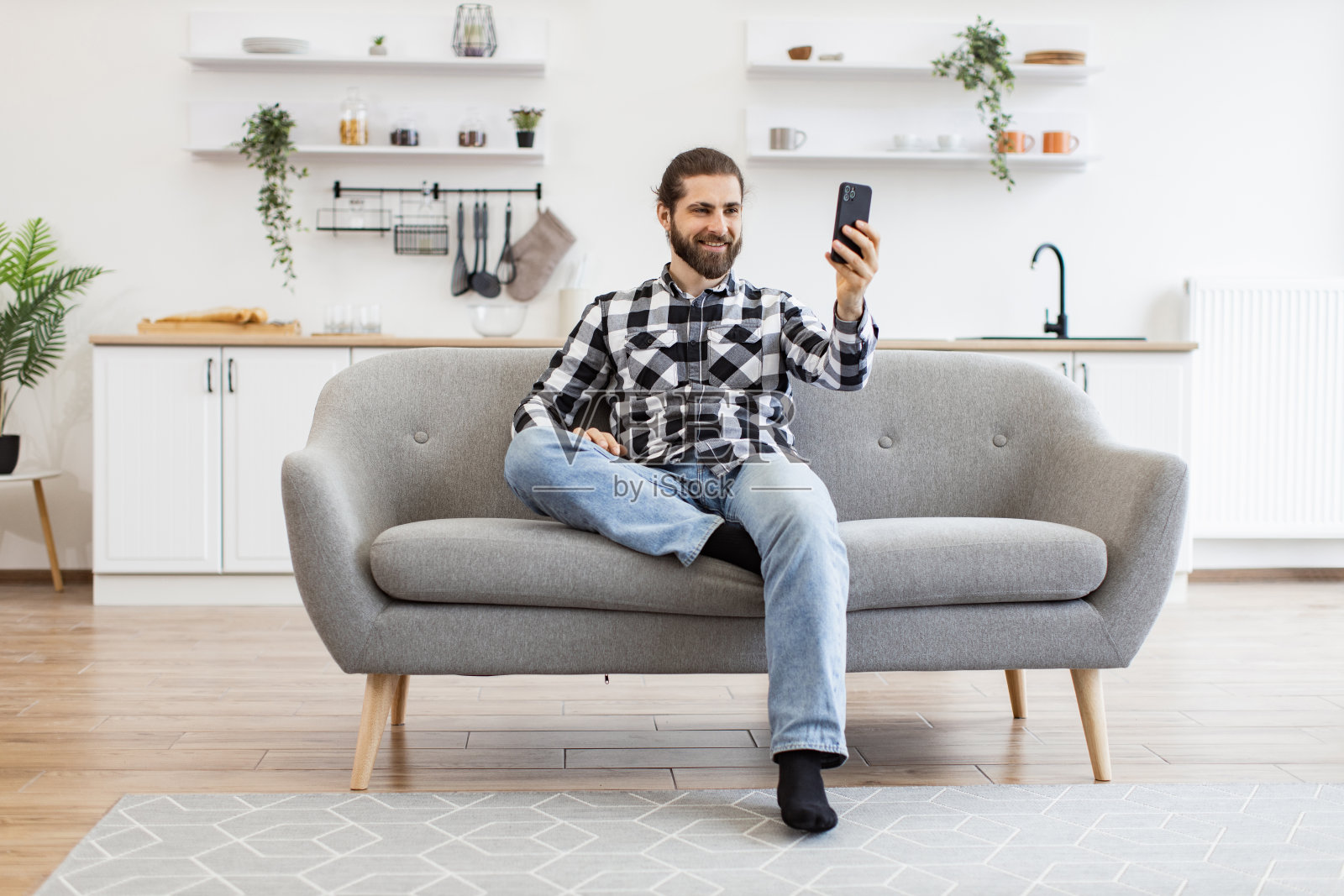 有魅力的年轻人拿着手机，通过厨房的网络摄像头说话。照片摄影图片