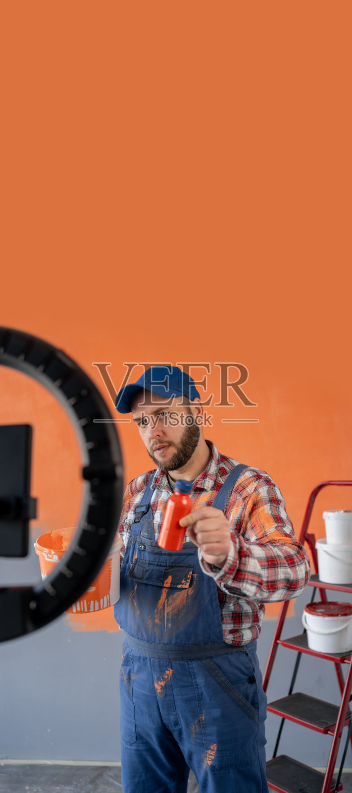 男工人油漆工博主拿着环形灯和智能手机在家里串流，录下涂墙、拿颜料和橙色颜料的视频。写博客，科技，装修房子照片摄影图片