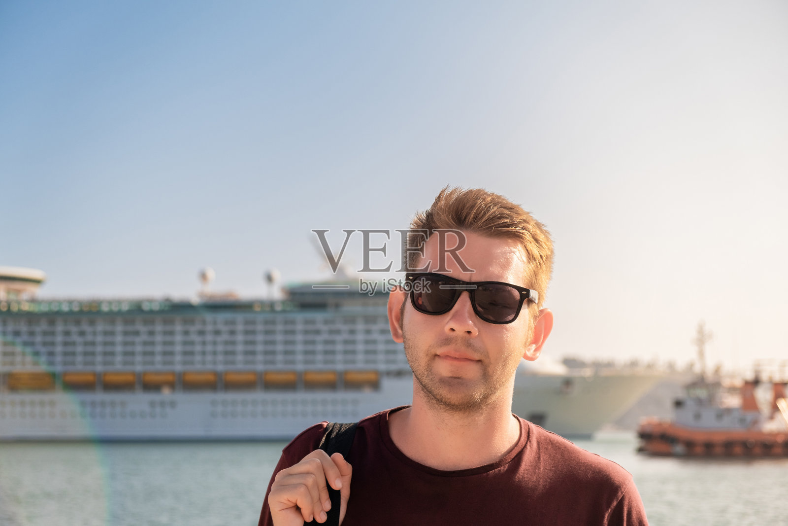在亚得里亚海的黑山巴尔港，一名戴着墨镜的游客站在大型游轮前的肖像。夏季邮轮假期照片摄影图片