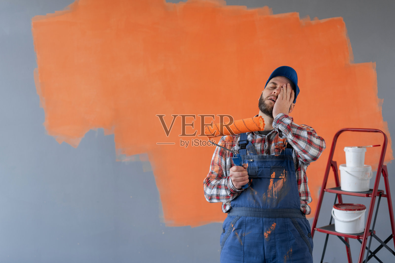 画家大胡子男子拿着滚轮，在橙色背景上带着惊讶的面部表情。照片摄影图片