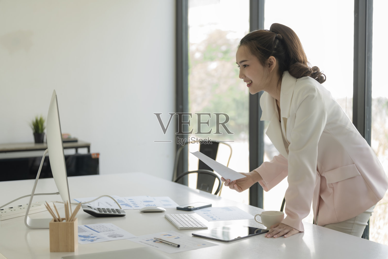 美丽的亚洲女商人拿着一张纸，在工作中使用电脑。照片摄影图片