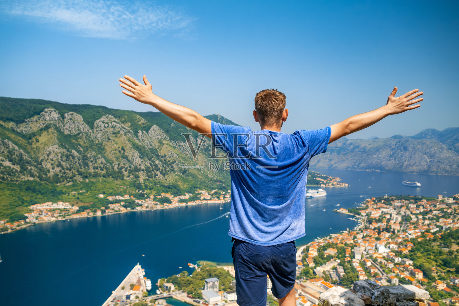 一名游客站在洛文斯山上，俯瞰科托尔湾和老城区，举起双手，黑山。徒步旅行后欣赏亚得里亚海峡湾美景的男性旅行者照片摄影图片