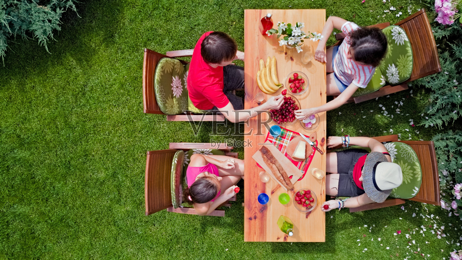 家人和朋友在公园的夏日花园聚会上一起在户外吃饭。从空中俯瞰草地上摆满食物和饮料的桌子。休闲、度假、野餐的概念照片摄影图片