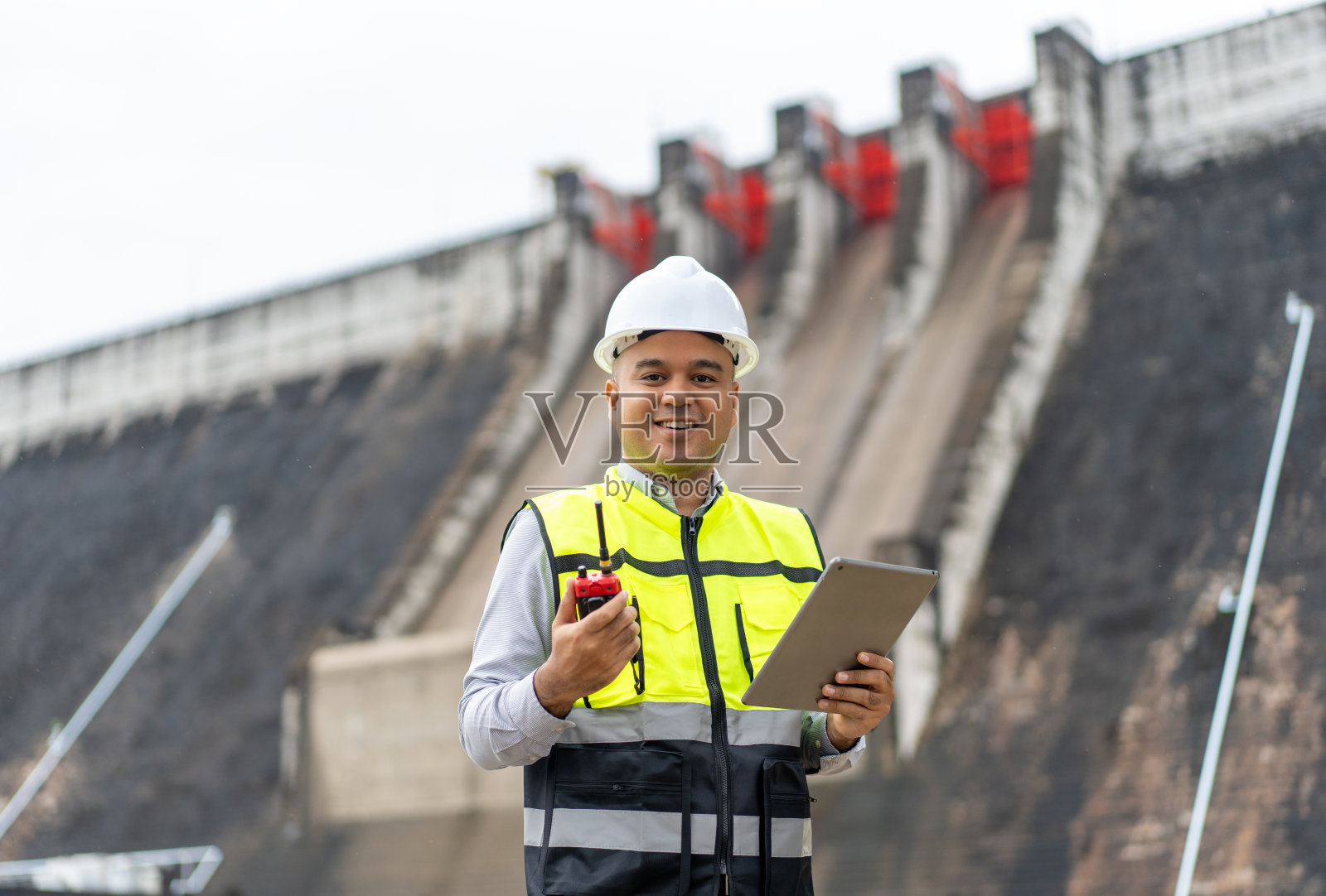 专业的亚洲维修工程师，头戴安全帽，在水电站大坝和灌溉工地工作。经理工程师在大型建筑项目中使用平板电脑。照片摄影图片
