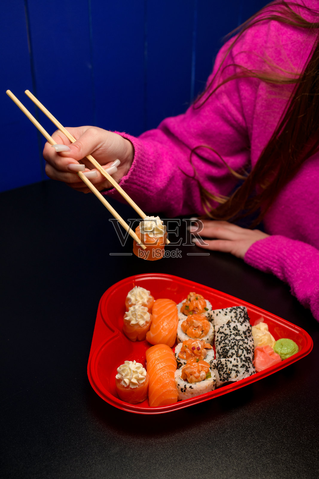 一个心形的盘子里装着面包卷，一个穿着粉色夹克的女孩坐在一张黑色的桌子旁照片摄影图片