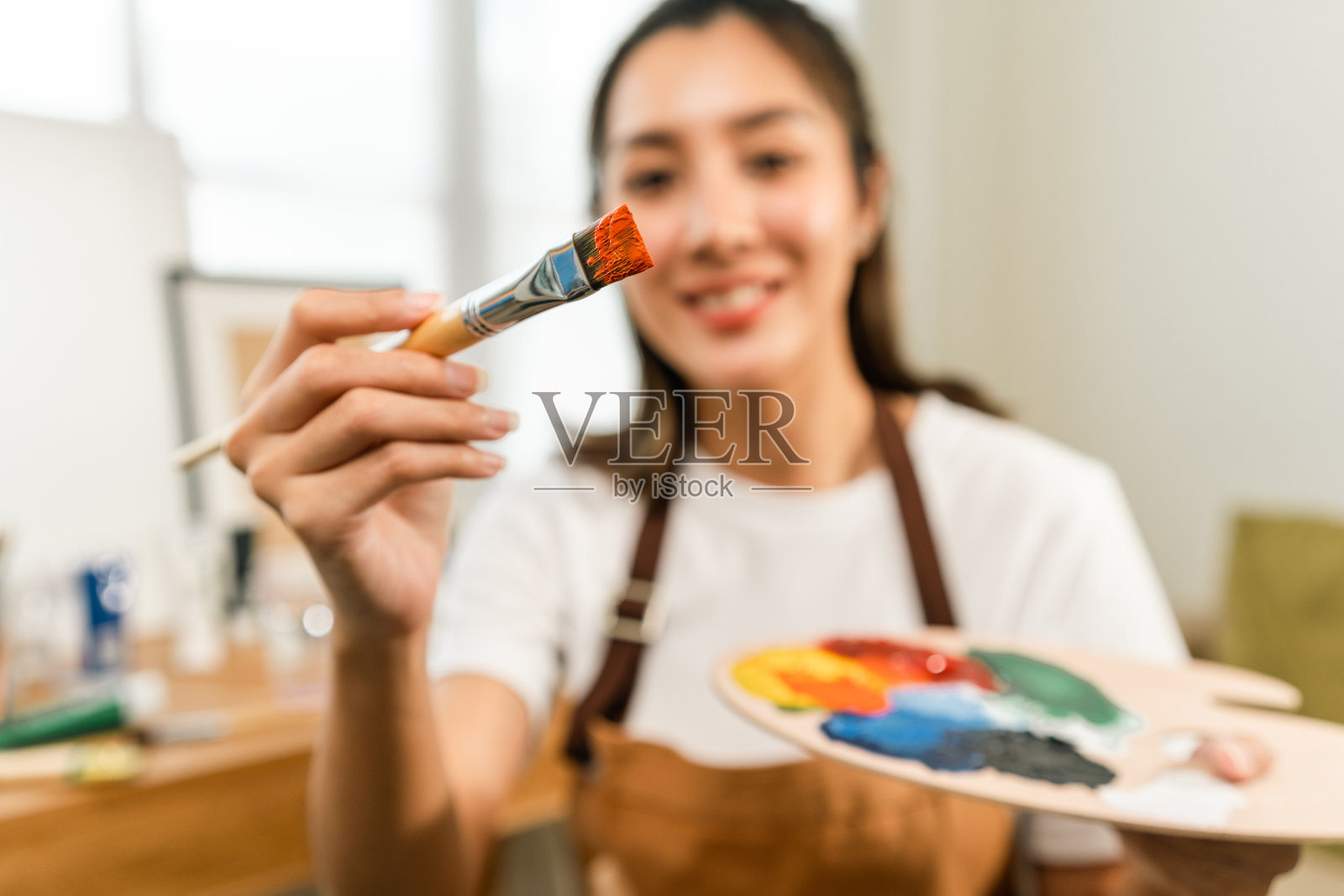 亚洲女艺术家正在用画笔和不同的丙烯酸颜料作画。作为艺术概念的女艺术家在创作工作室的画布上作画照片摄影图片