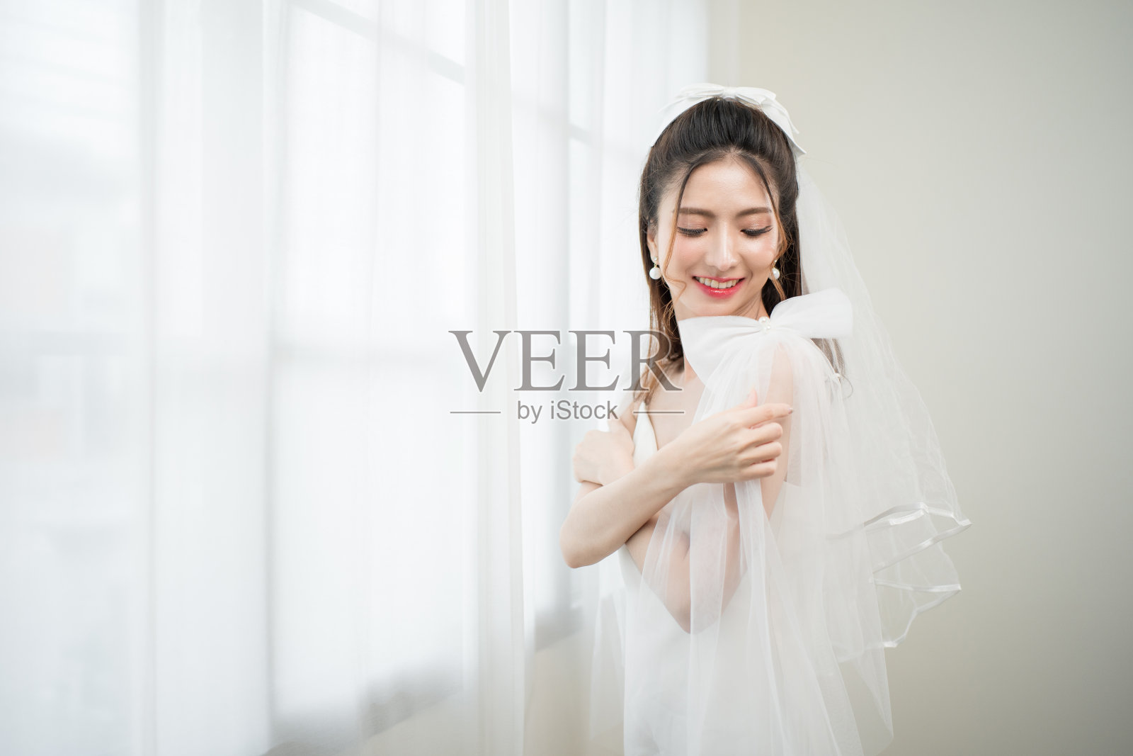 美丽的亚洲新娘与时尚的婚礼发型和化妆。年轻美丽的新娘的肖像在白色的房间里拍摄的婚礼工作室。照片摄影图片