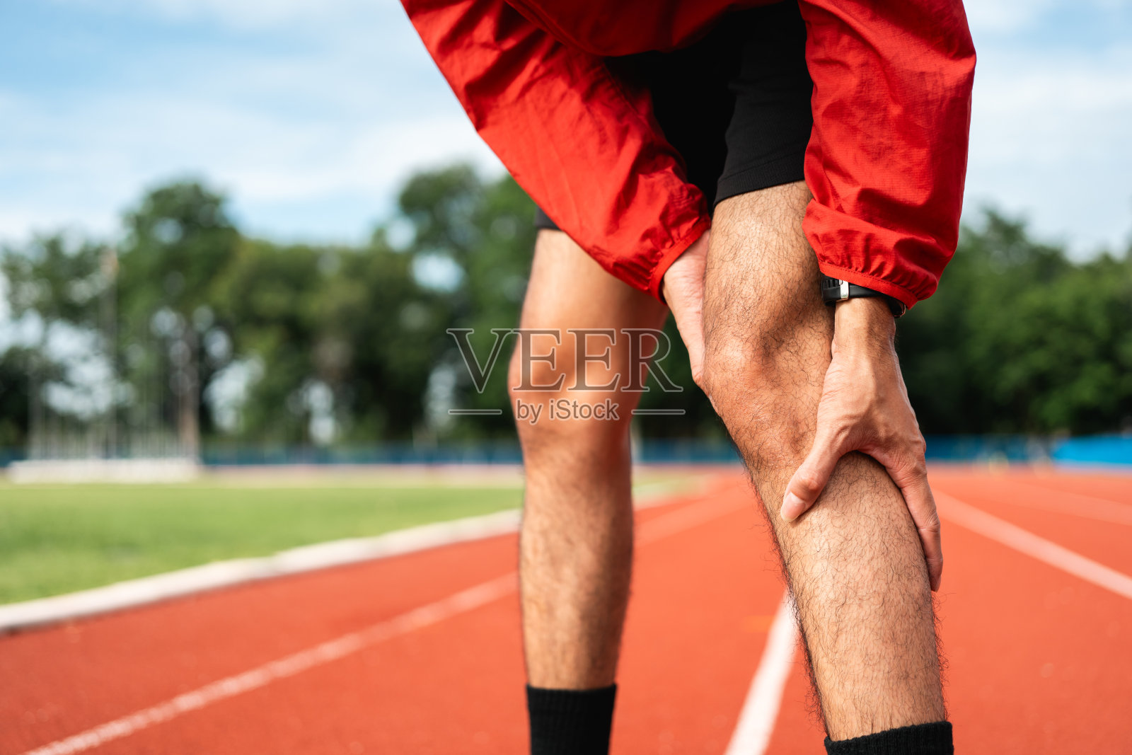 一个年轻人在运动场的跑道上慢跑时很累。跑步者膝盖酸痛，因为他跑得太久了。锻炼直到受伤。训练运动员在户外锻炼。照片摄影图片