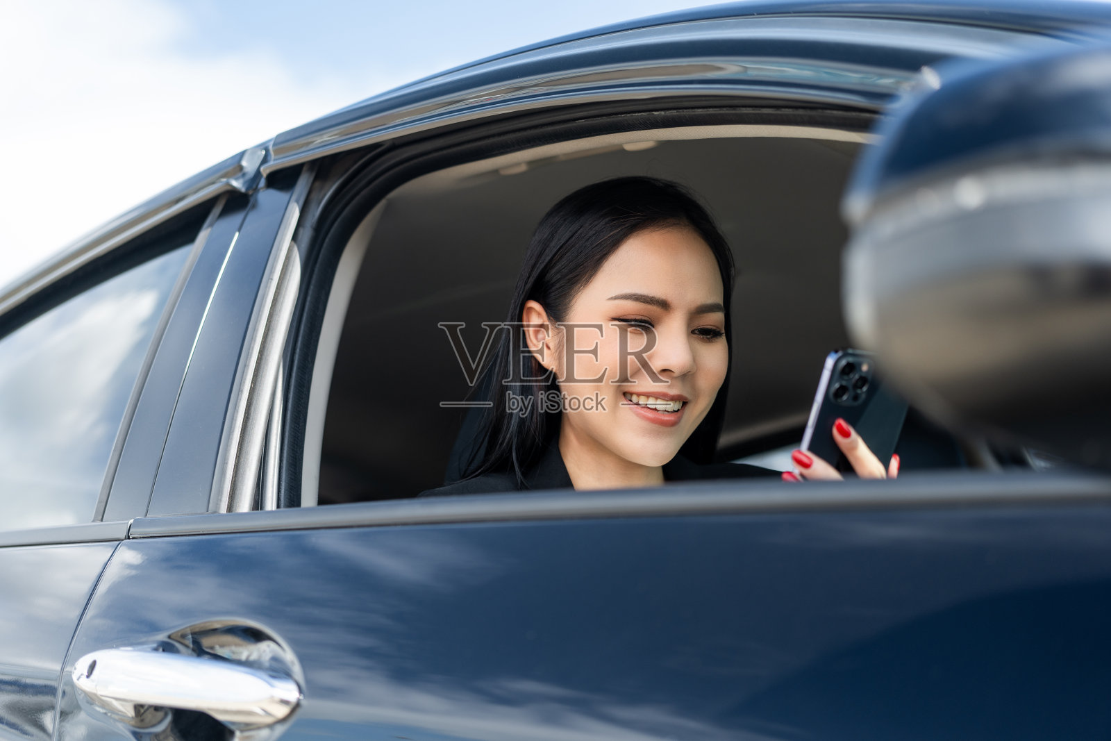 年轻漂亮的亚洲女商人一边开车一边用智能手机买新车。她非常高兴和兴奋与手机驾驶应用程序。商务女车在路上照片摄影图片