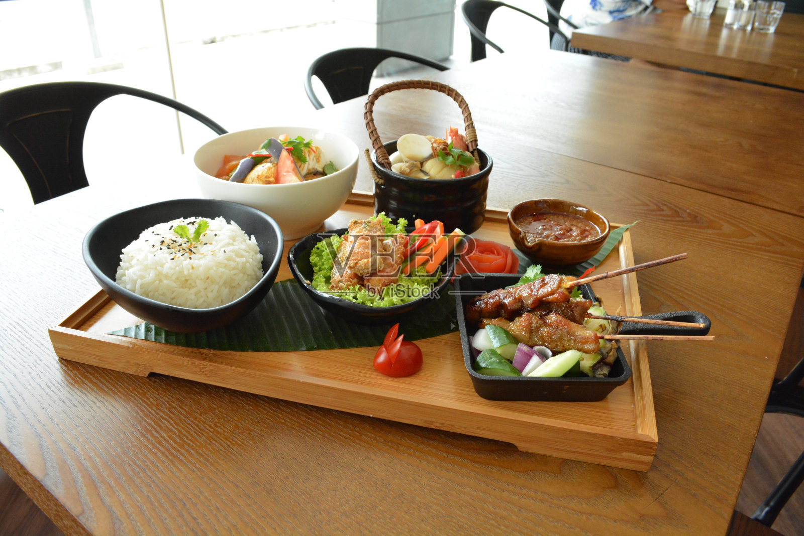 亚洲便当聚会，包括海鲜汤，油炸小吃，沙爹鸡和花生辣酱，炒菜和蒸白米饭在木板托盘亚洲清真菜单照片摄影图片