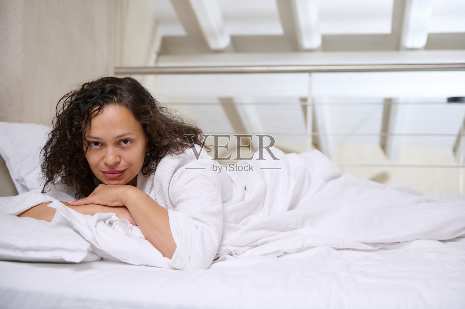 可爱迷人的漂亮女人穿着白色华夫格浴袍，在白色的床单上放松，早上醒来照片摄影图片