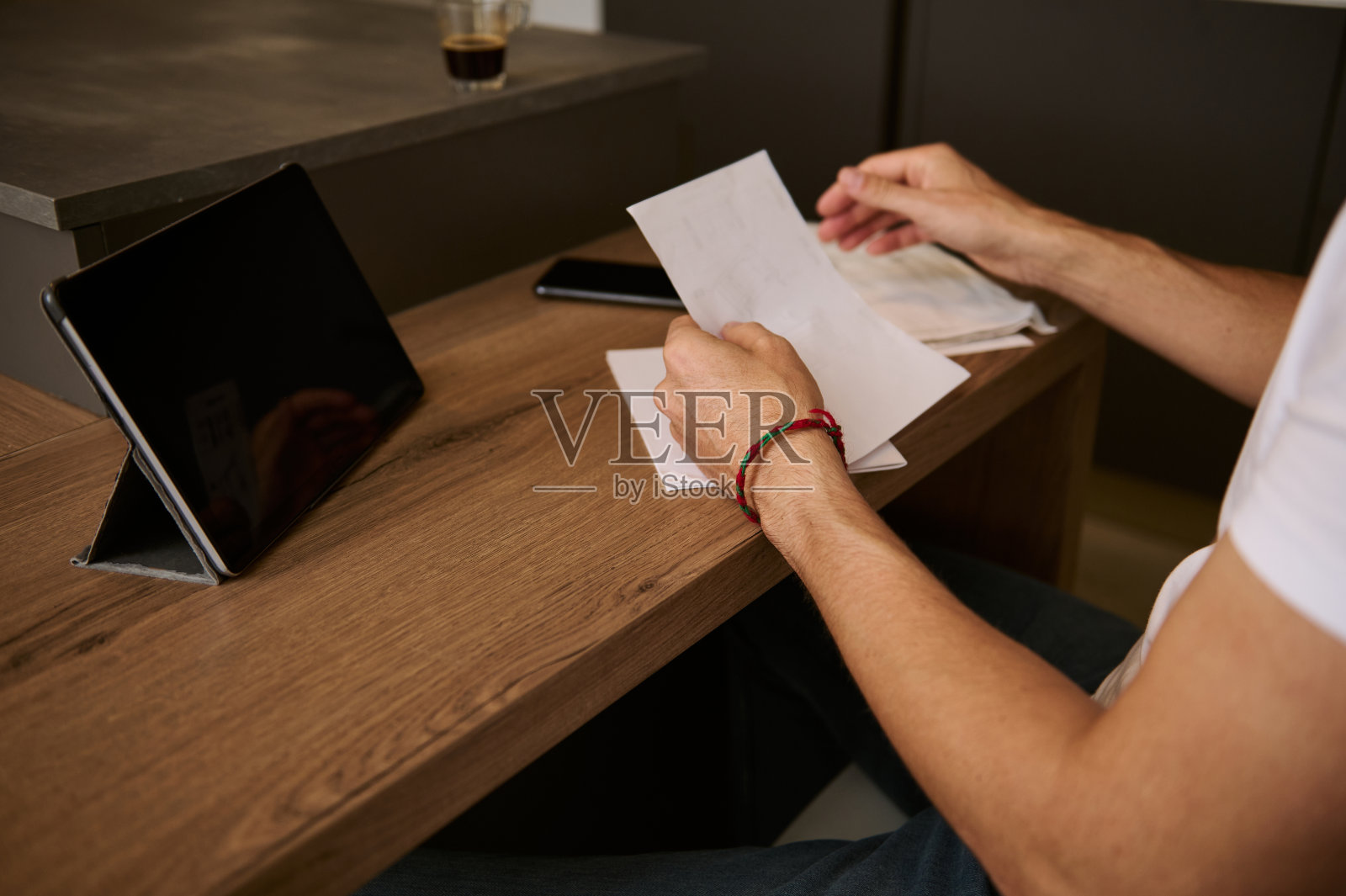 一个男人坐在家里的办公室里，手里拿着账单，用平板电脑在线支付。电子银行的概念。照片摄影图片