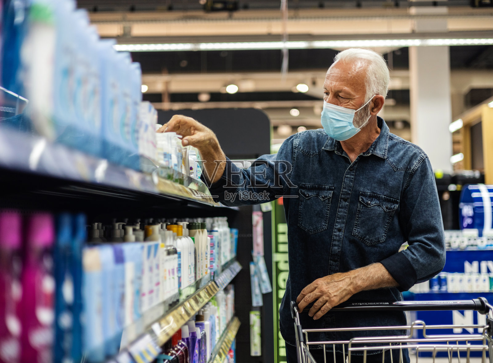 一名男子戴着口罩在超市购物。白人男子在超市购物时戴着口罩，一边推着购物车，一边避免感染病毒，生活方式观念。照片摄影图片