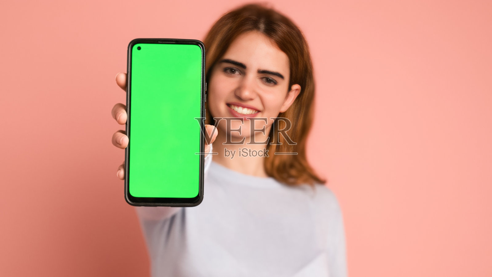 快乐的女人在工作室展示带chromakey的智能手机照片摄影图片