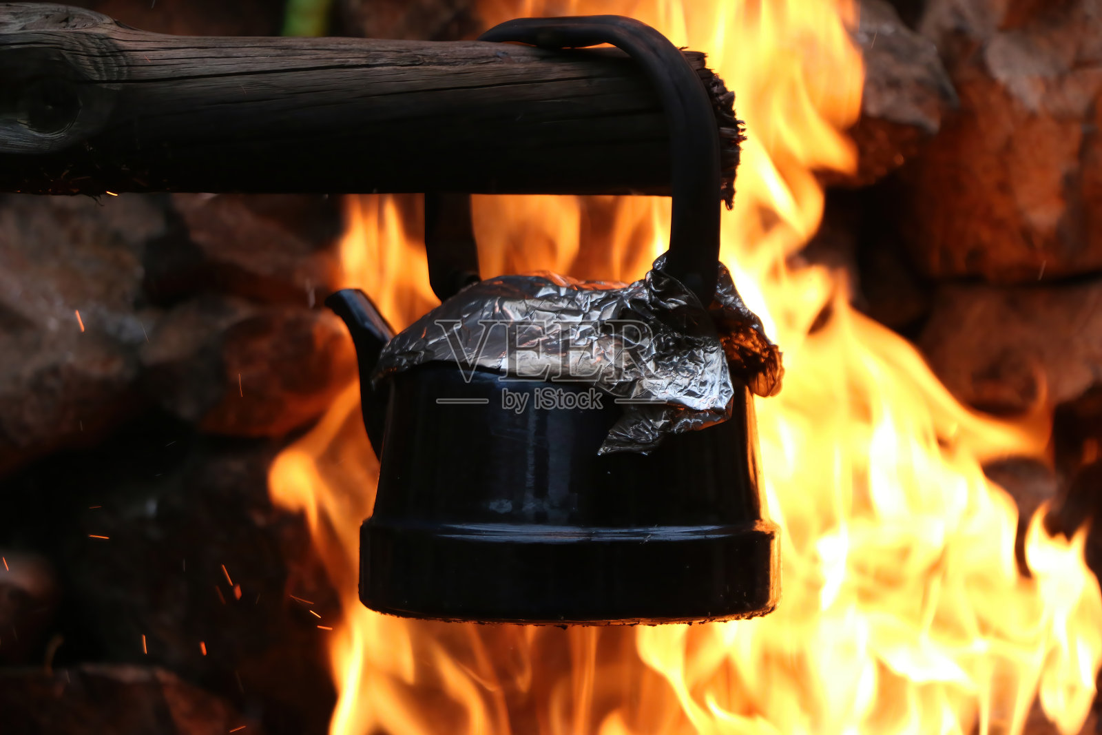 一个灰色的水壶在篝火上烧着，周围有火焰。照片摄影图片