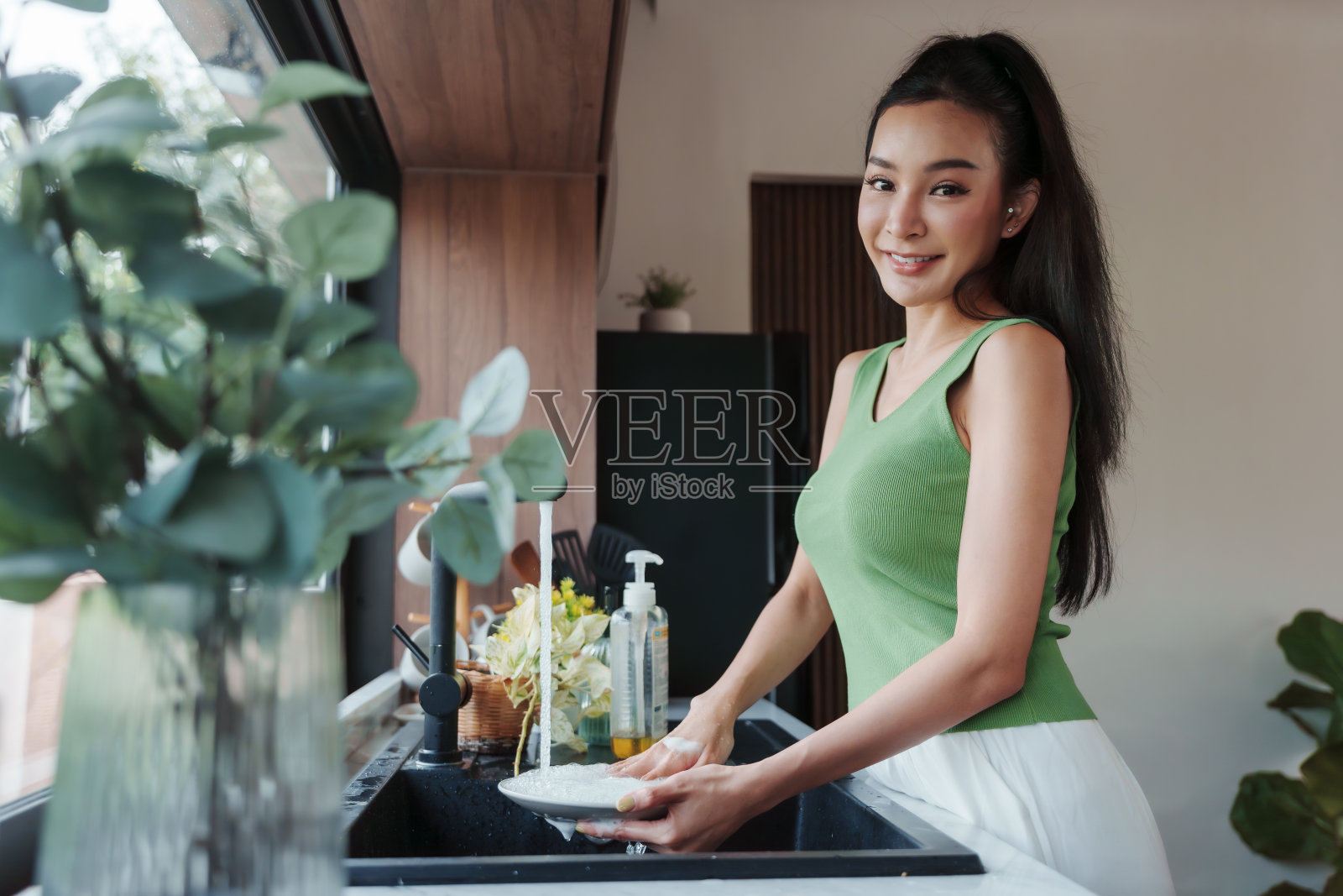 在明亮的厨房里，一位快乐的女士微笑着洗盘子照片摄影图片
