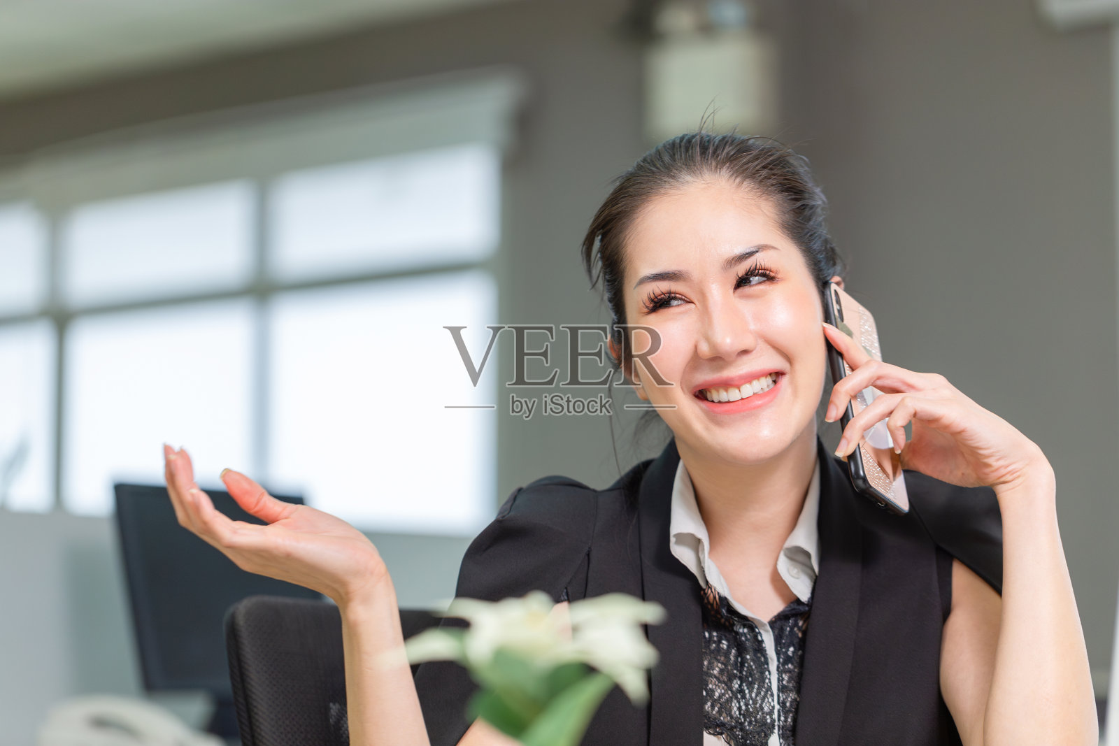 微笑的年轻女子在办公室工作和使用电话。兴奋的漂亮女孩在办公室使用智能手机照片摄影图片