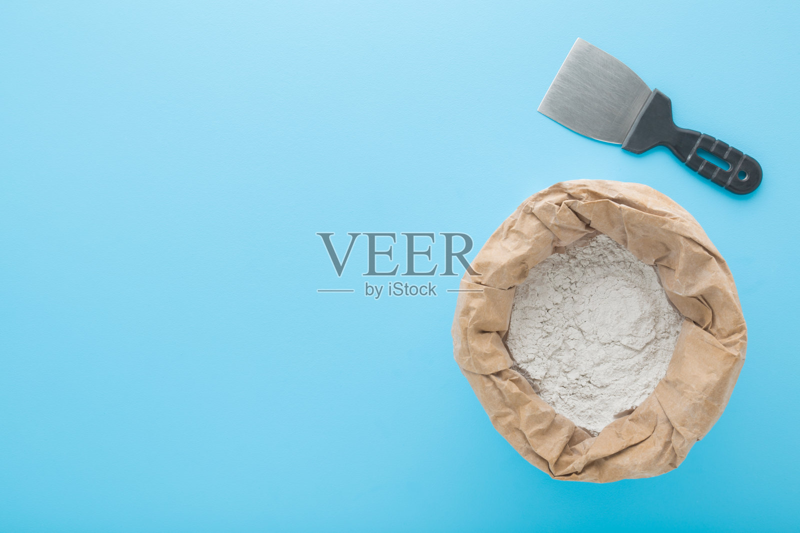 抹刀和打开的纸袋白色干整理腻子抹灰天花板和墙壁表面在淡蓝色的桌子背景。家里的维修工作。特写镜头。空白位置用于文本。自顶向下视图。照片摄影图片