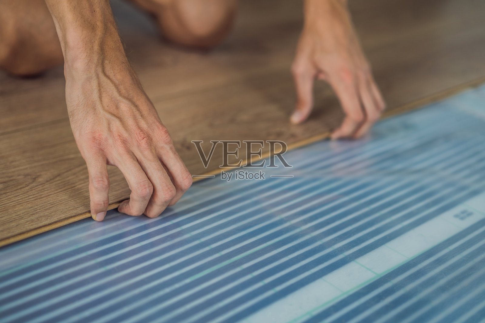 男子在暖膜地板上安装新的强化木地板。强化地板下红外线地暖系统照片摄影图片