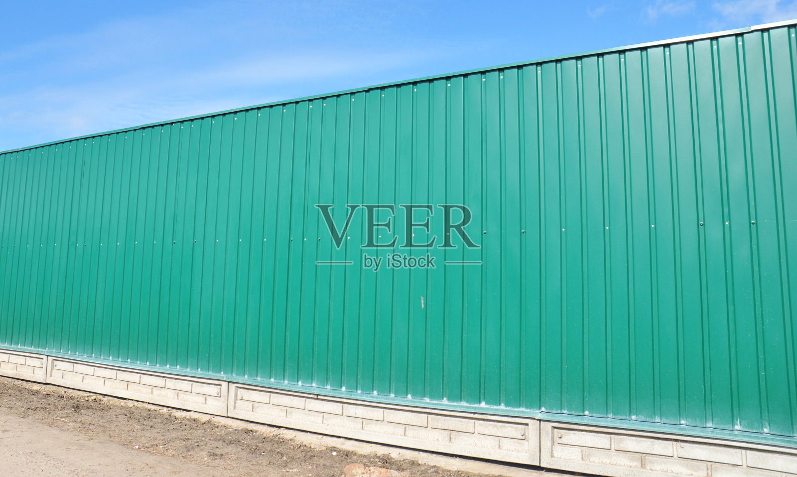 绿色金属栅栏板安装在砖基础上，对着蓝天。照片摄影图片