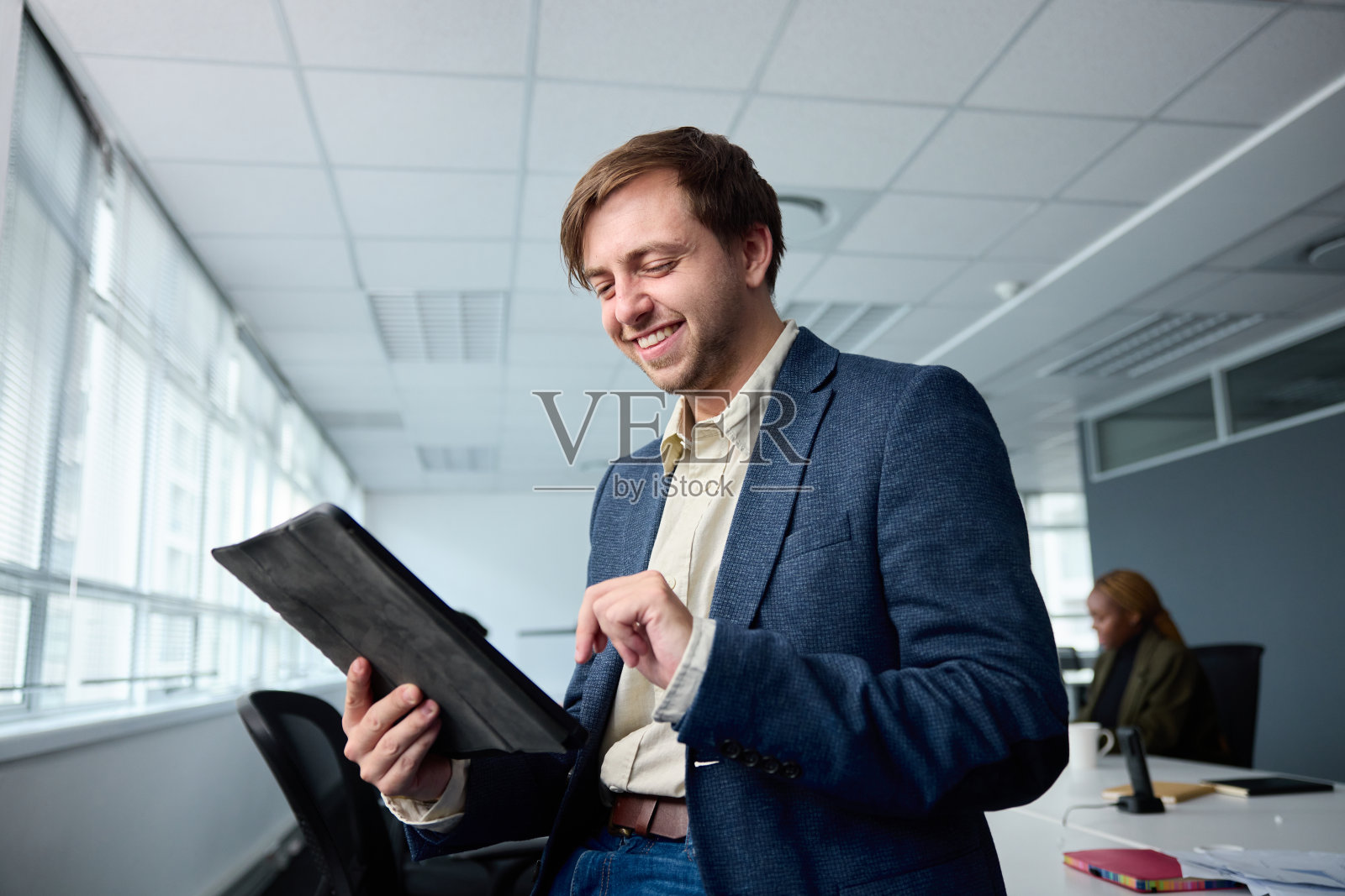 快乐的年轻商人穿着商务装，在办公桌前与同事一起使用数字平板电脑照片摄影图片