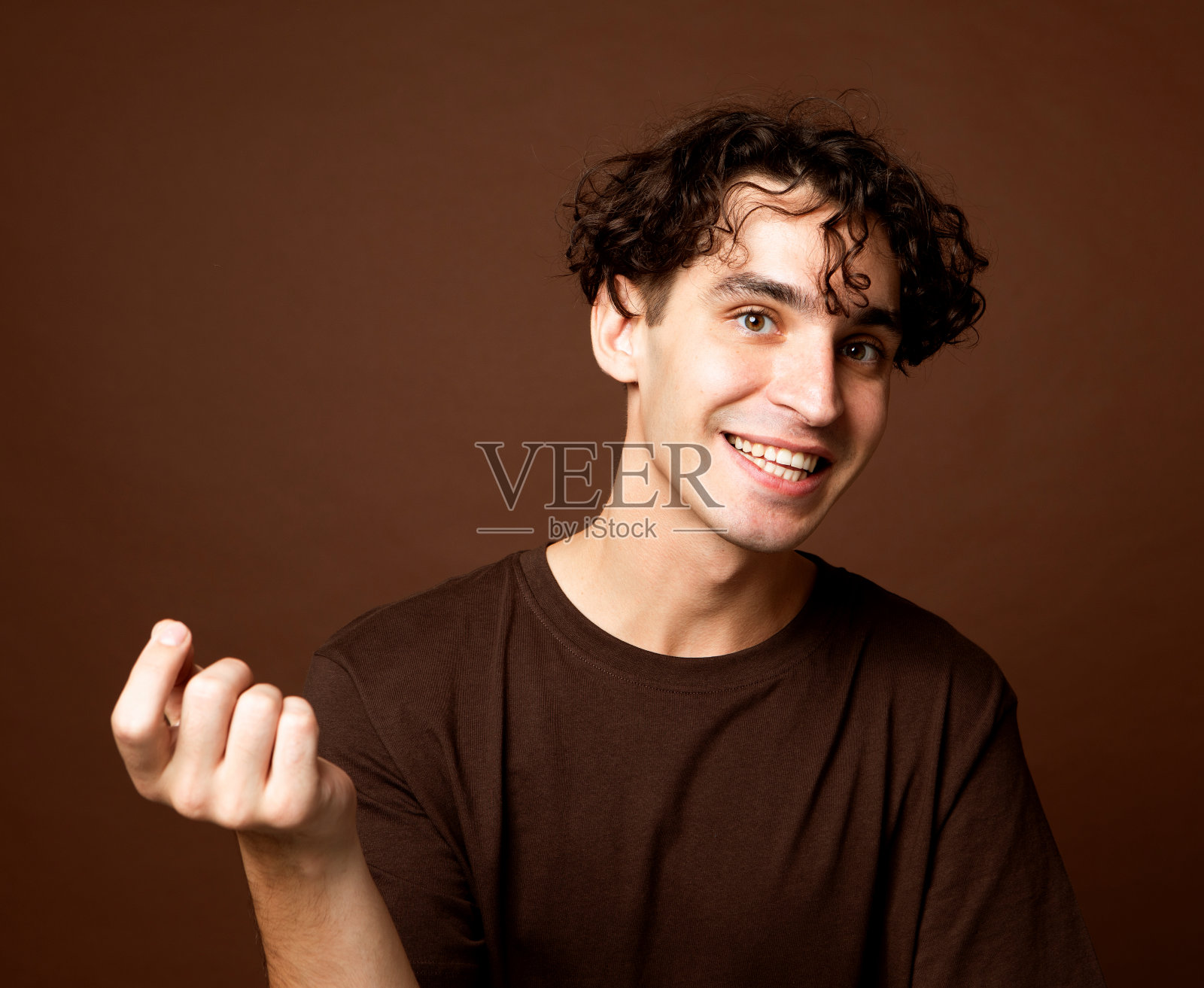 穿着棕色t恤、面带微笑的英俊年轻人看着棕色背景下的镜头照片摄影图片