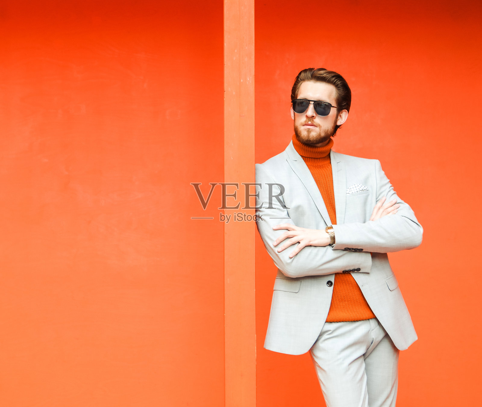 一个时髦的年轻人，穿着橙色的毛衣和夏日西装，戴着太阳镜，在夏日的橙色墙壁的背景下。照片摄影图片