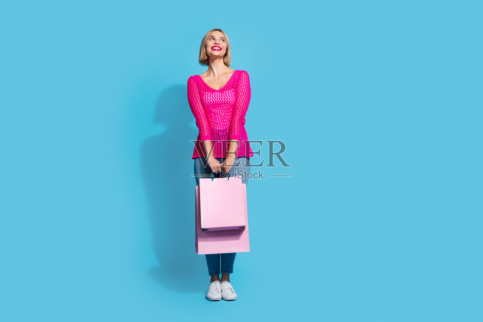 漂亮的年轻女孩的全尺寸照片购物袋看空空间穿时髦的粉红色针织服装孤立的蓝色背景照片摄影图片