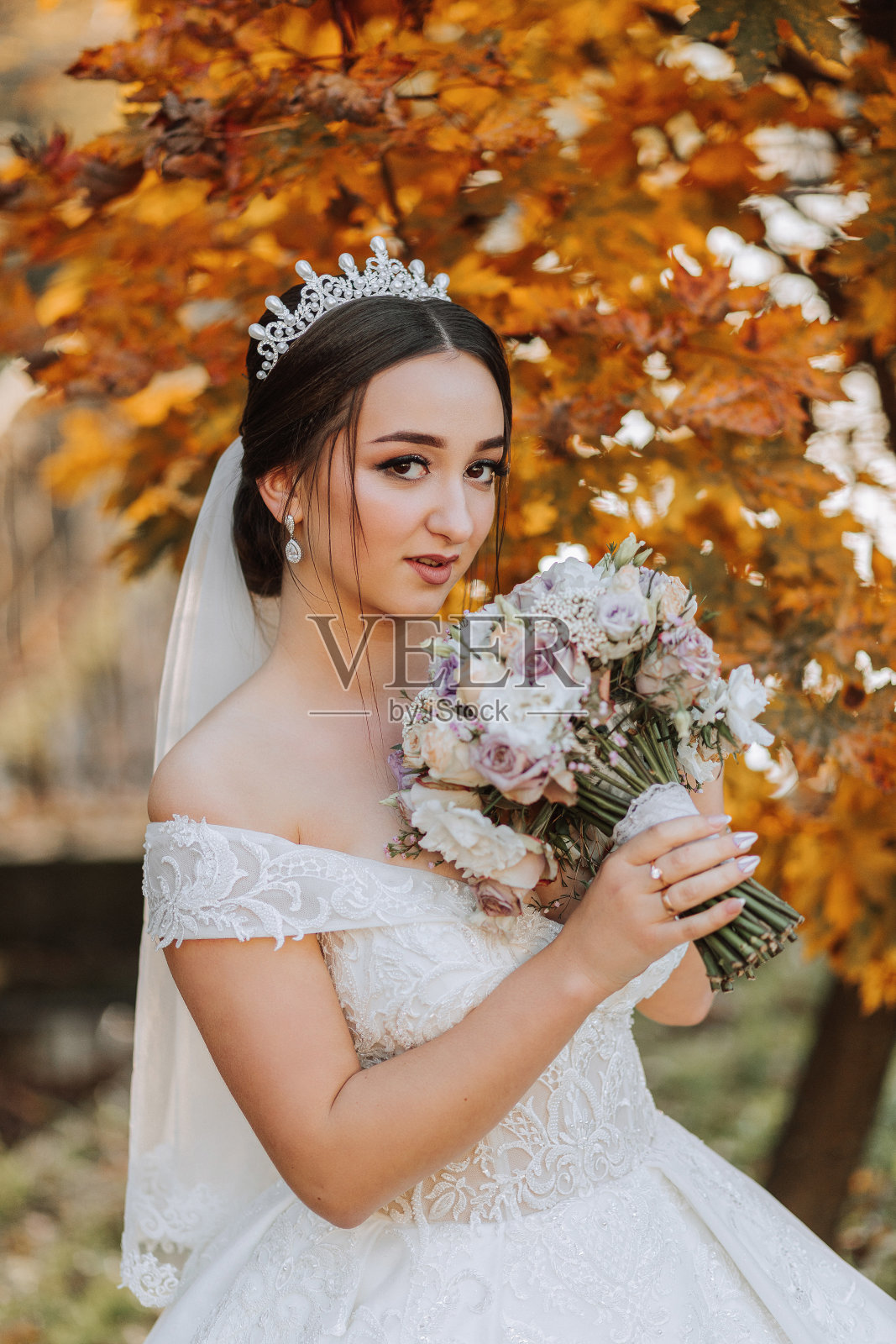 一位美丽的新娘手持一束鲜花站在秋叶旁的大自然中。一位年轻新娘的特写婚纱照。婚礼摄影。照片摄影图片