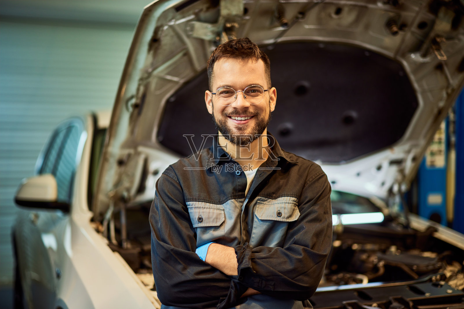 一个机械师站在打开的引擎盖前，对着镜头微笑。照片摄影图片
