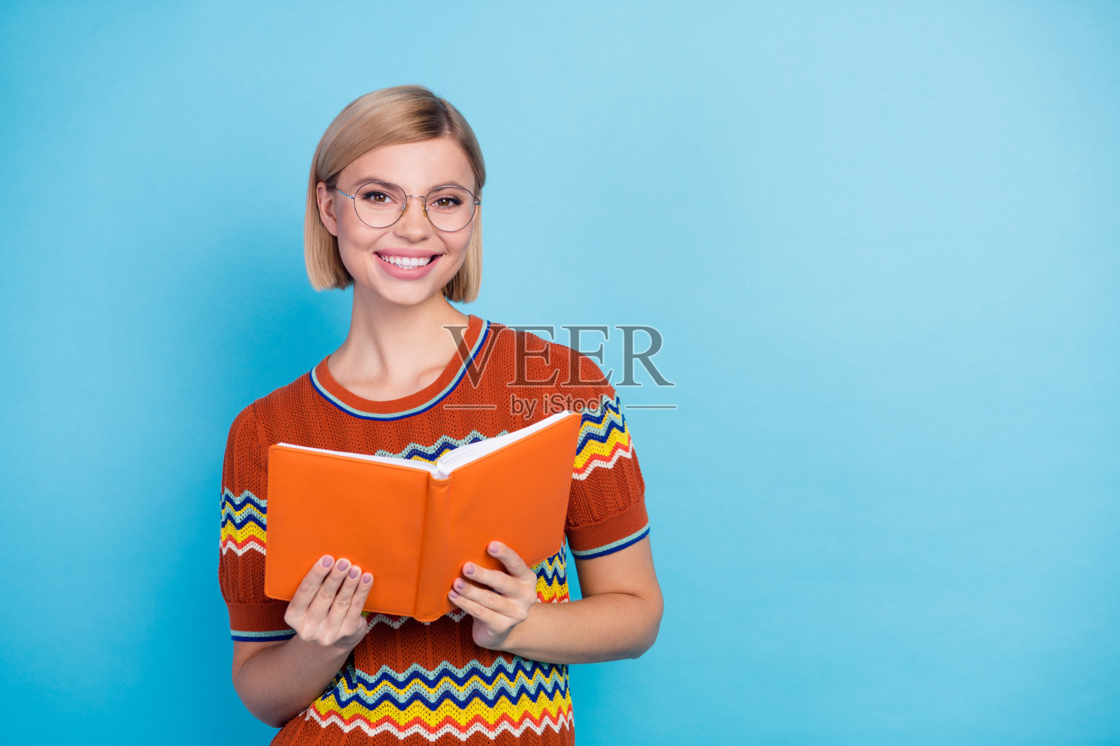 聪明女孩的肖像，短发，穿条纹t恤，戴眼镜，在图书馆读书，孤立的蓝色背景照片摄影图片