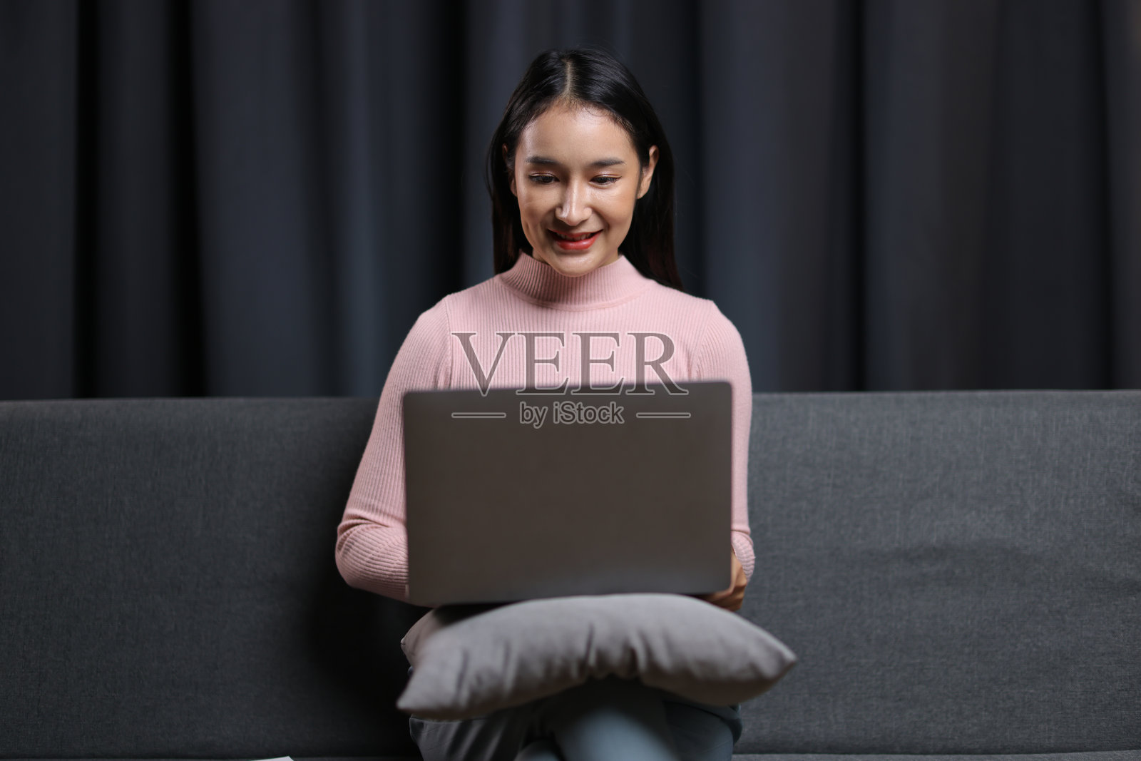 女人坐在家里的沙发上用笔记本电脑。照片摄影图片