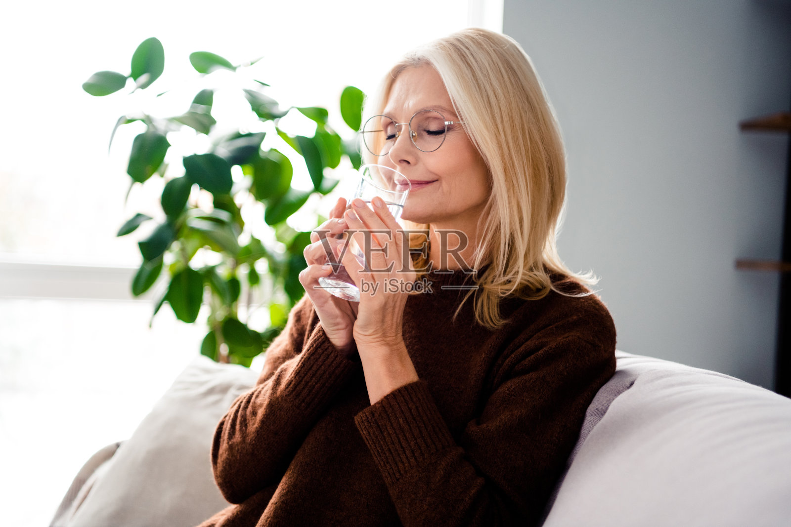 迷人、梦幻、可爱的退休女士坐在沙发上，在室内喝着清新干净的水照片摄影图片