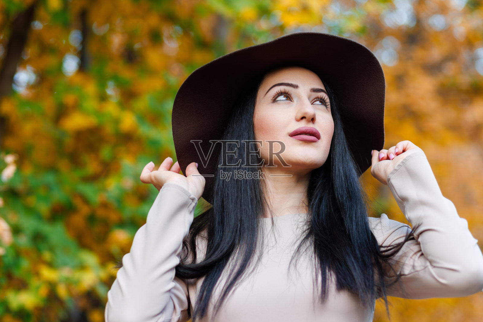 一个时髦的年轻女子的特写，宽边帽是她在低语的树叶中唯一的伴侣照片摄影图片