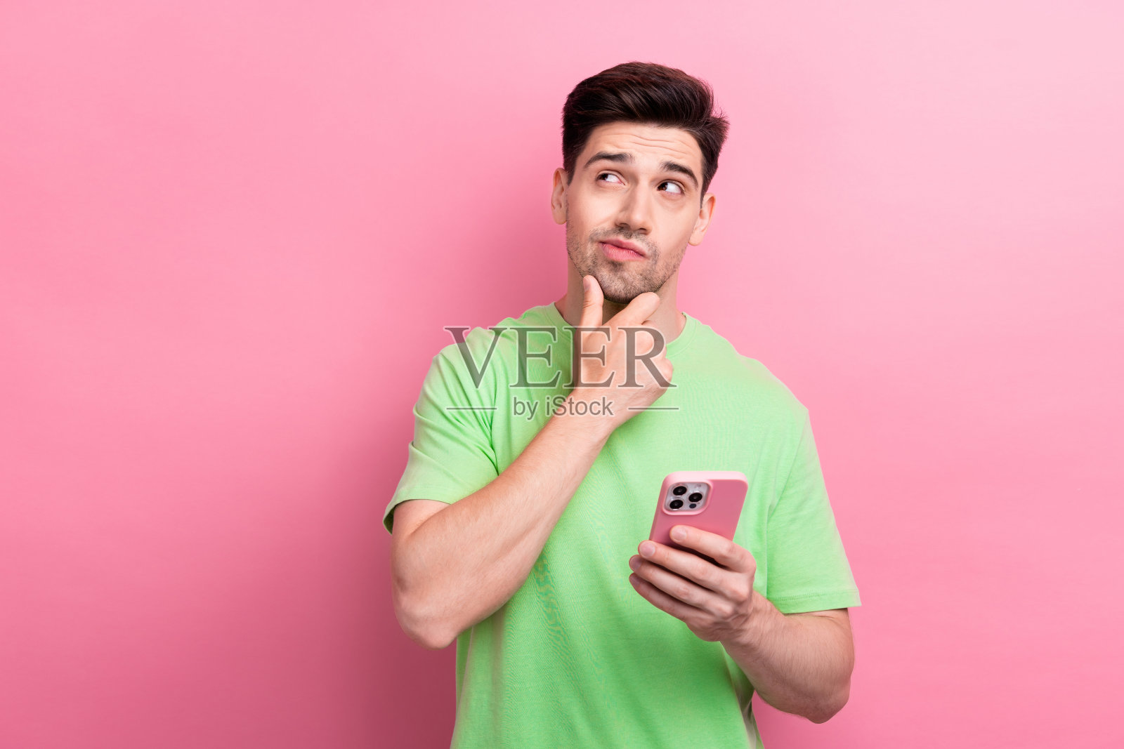 有头脑的好男人穿着时髦的绿色衣服，想买小玩意，在粉红色的背景上寻找孤立的空间照片摄影图片
