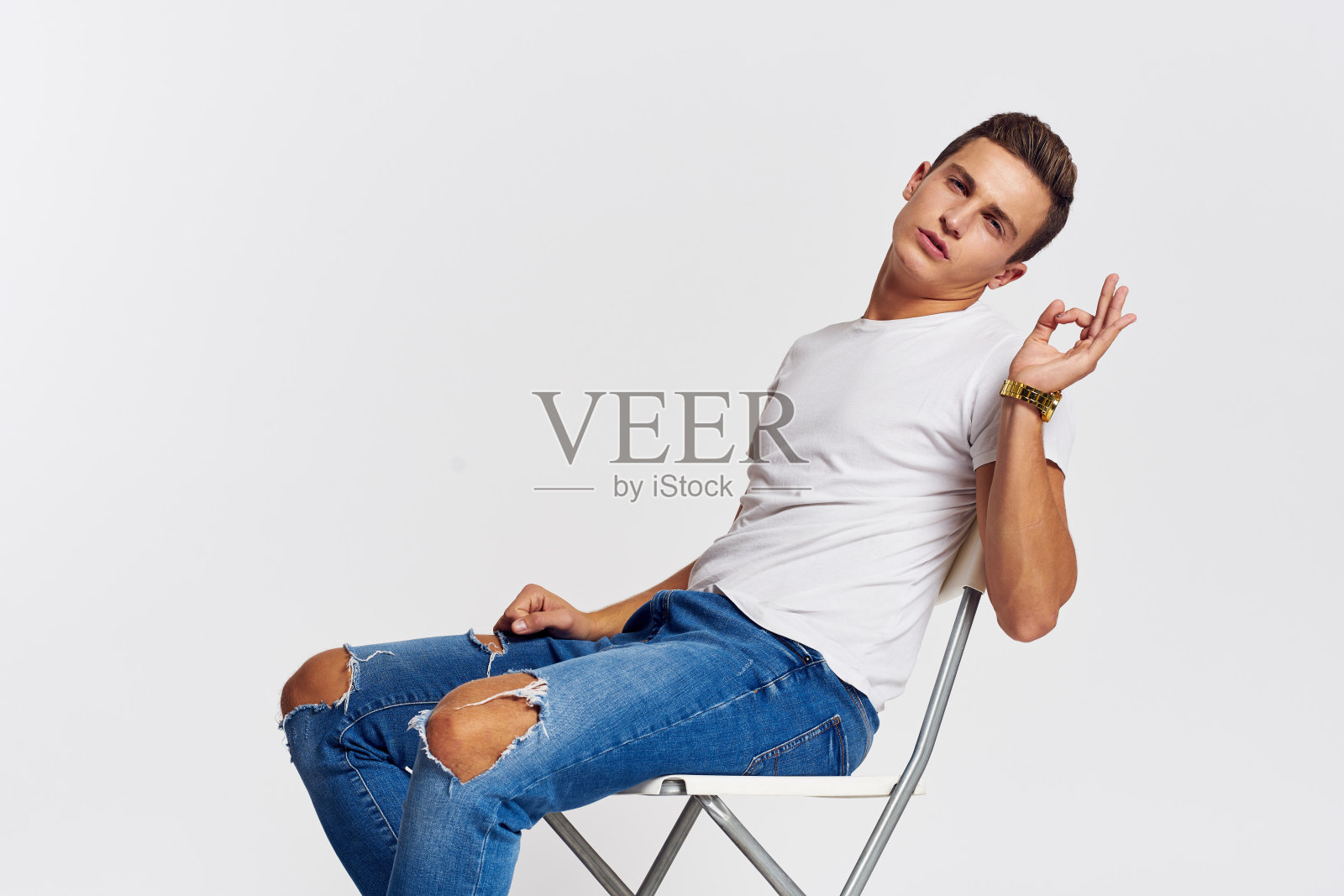 室内椅子上的男人撕破牛仔裤白t恤帅气的脸模特浅色背景照片摄影图片