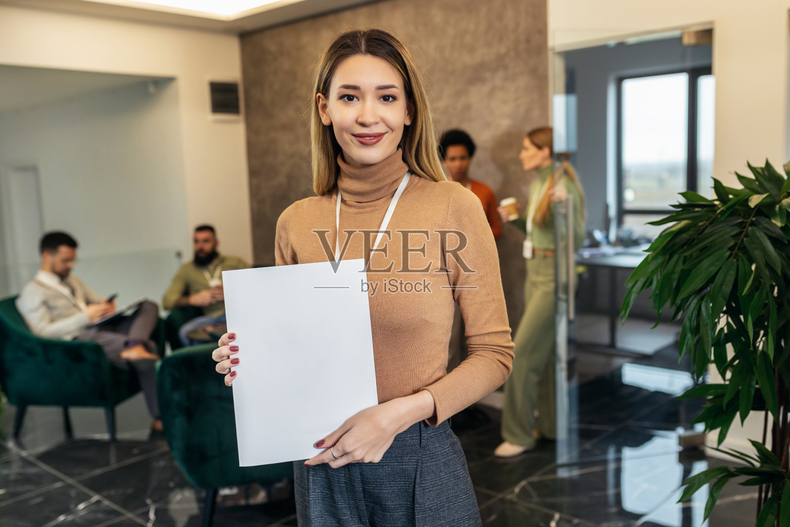 一位穿着随意的女商人站在办公楼的大厅里，面对着一个商业团队照片摄影图片