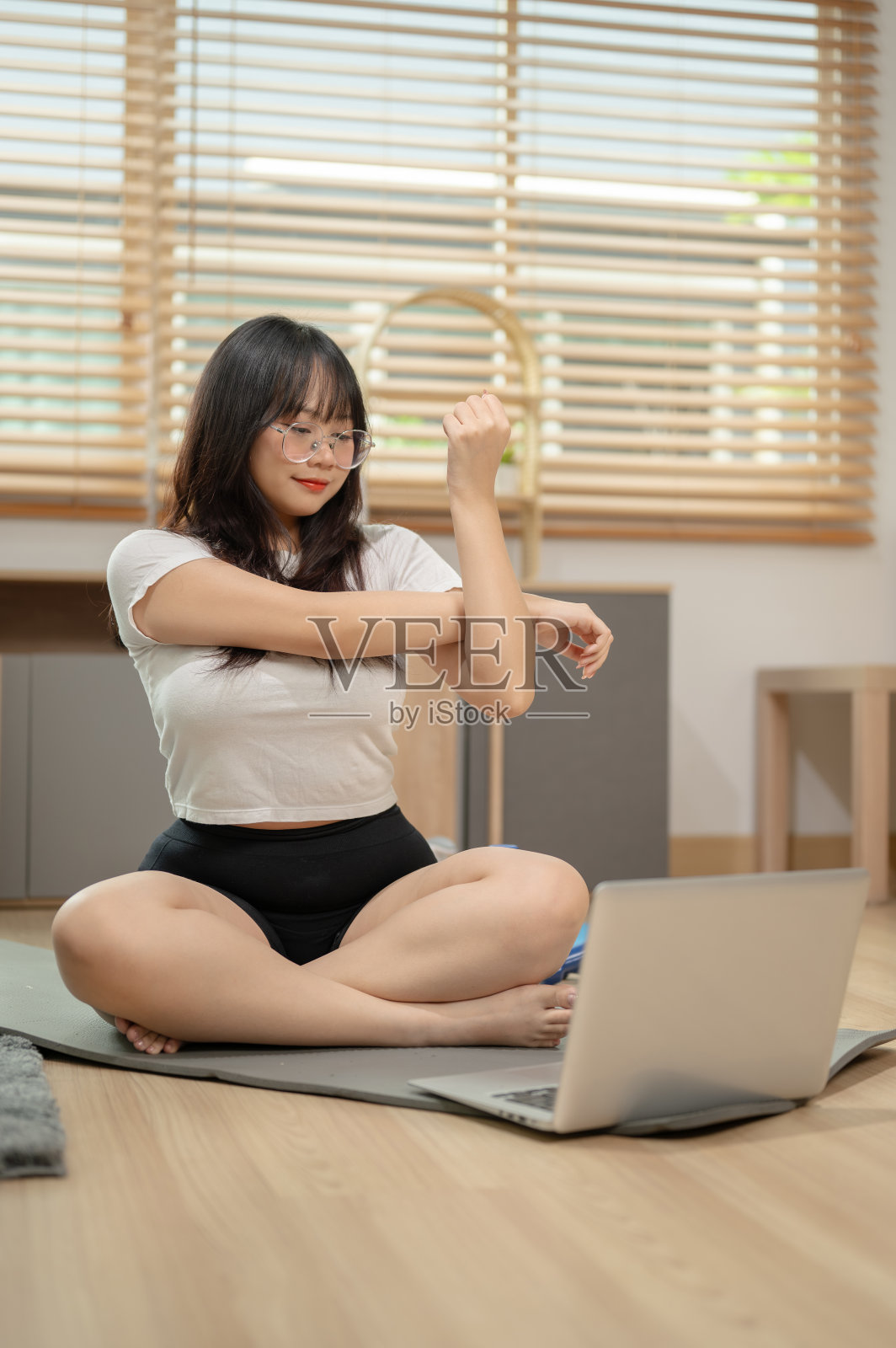 一位健康的女士正在瑜伽垫上伸展身体，同时观看在线瑜伽教程视频。照片摄影图片