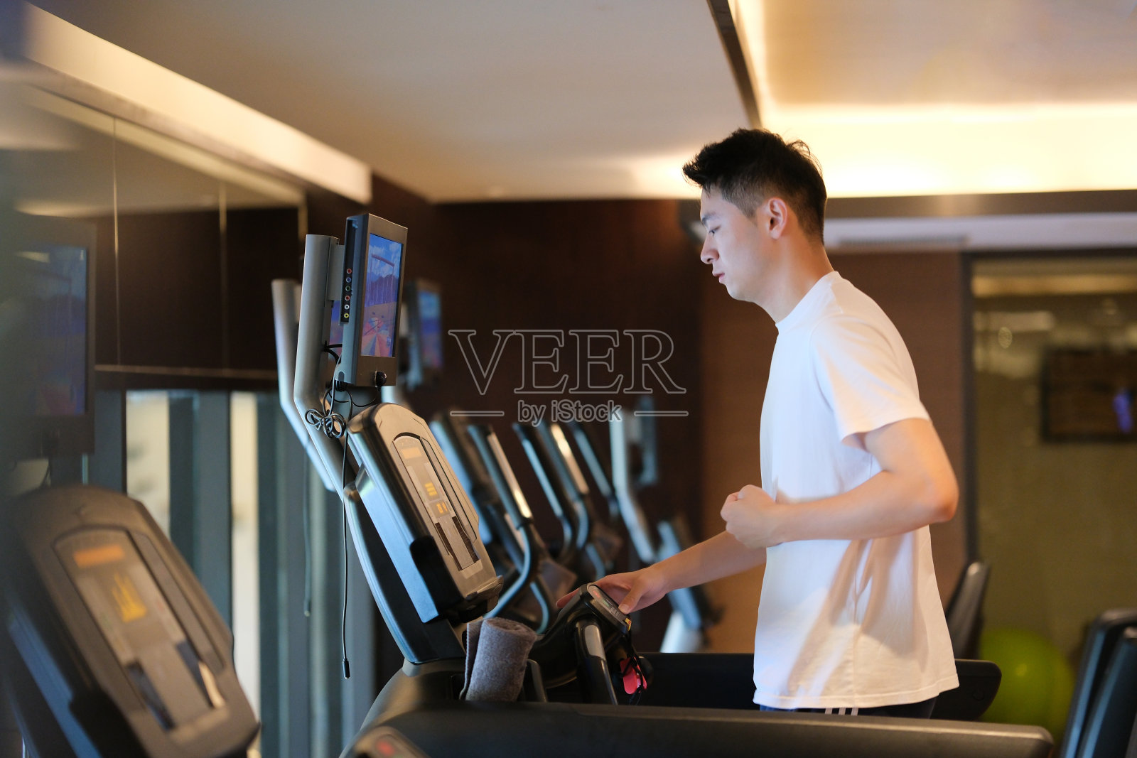 亚洲年轻人在室内健身房里的跑步机上跑步照片摄影图片